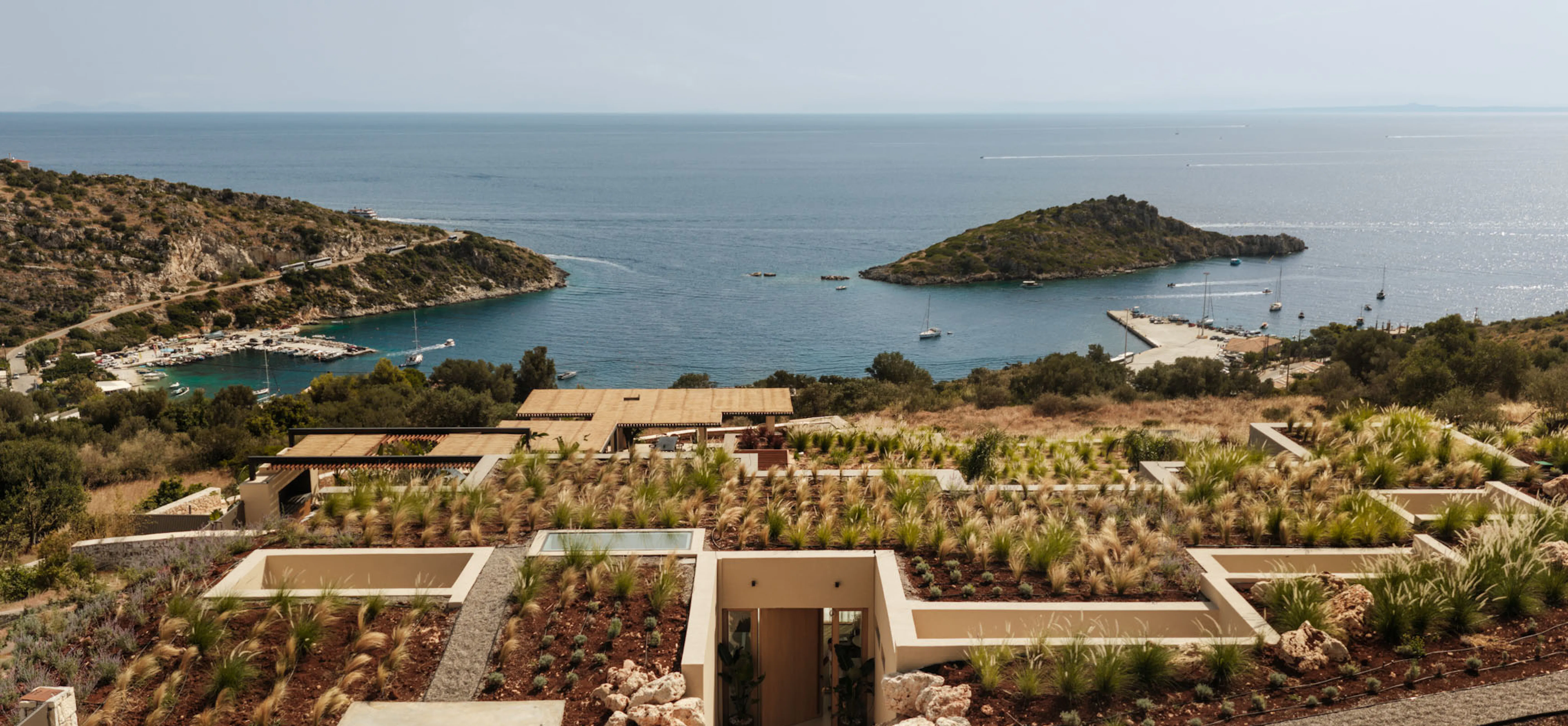 View from The Upper House across its sunken wildflower roof gardens to the bay below, with boats moored between two headlands and the sea beyond