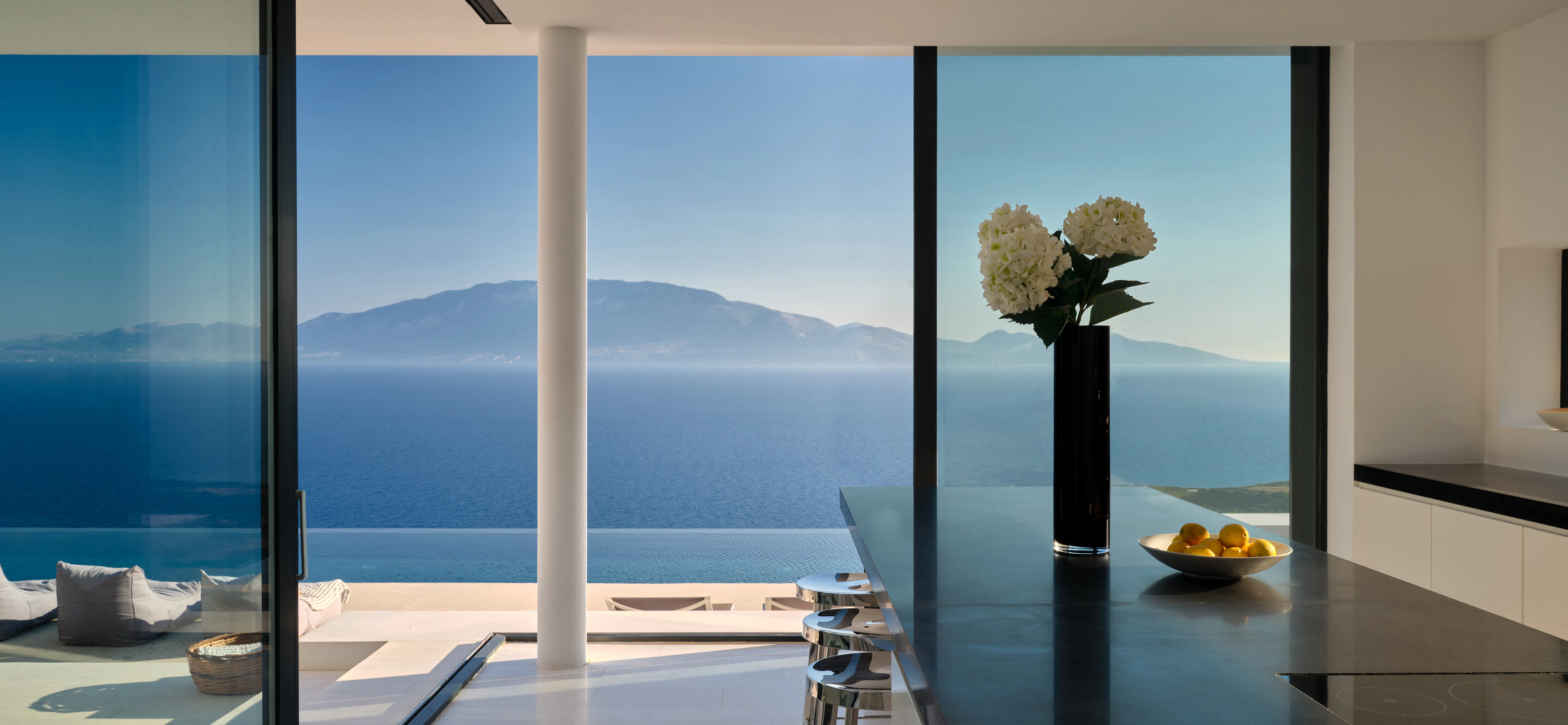 Terrace daybed with a folded striped throw, overlooking the sea beneath a clear blue sky
