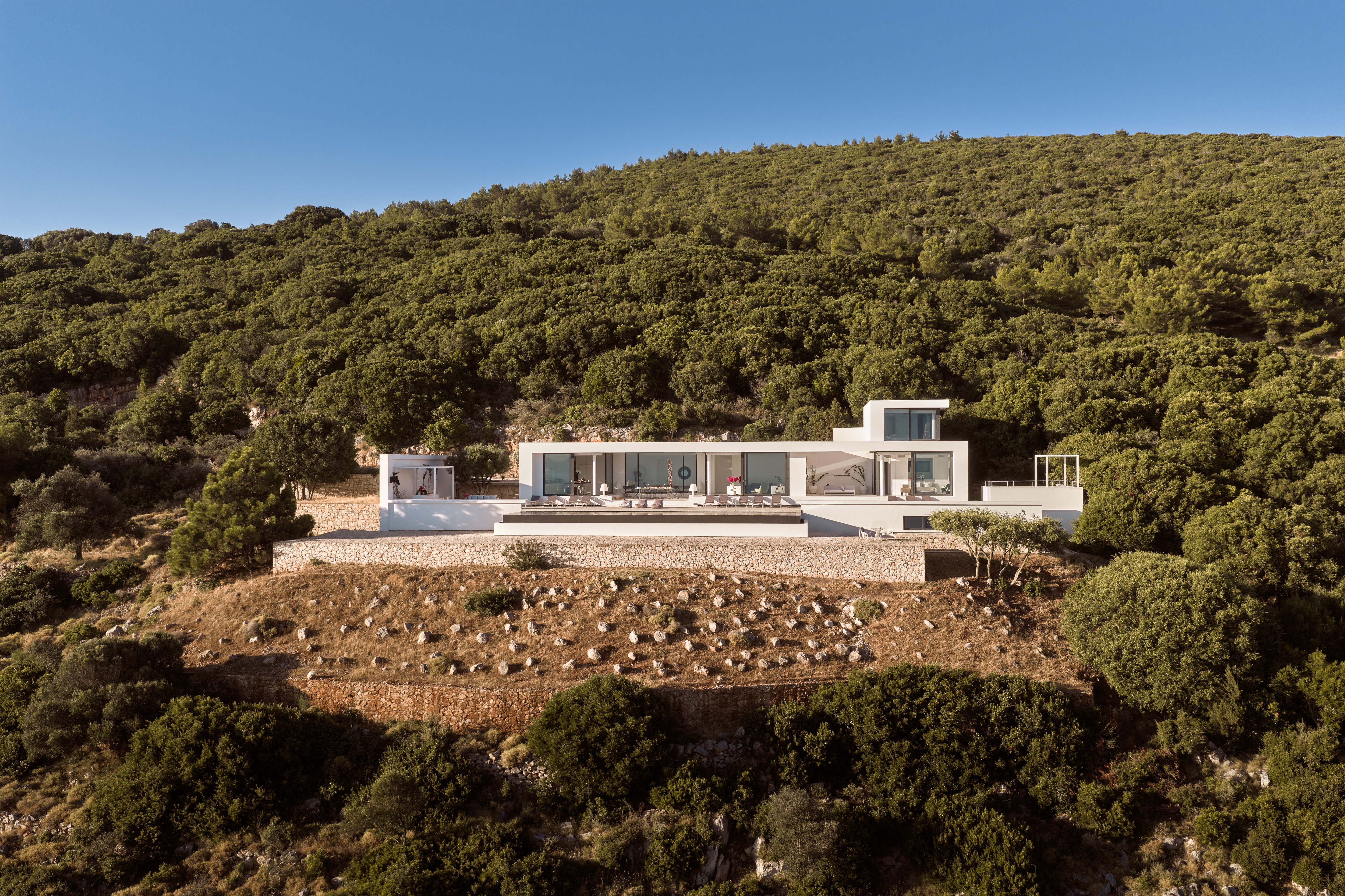 Aerial view of the villa surrounded by dense green hillside, showing the pool terrace and building layout