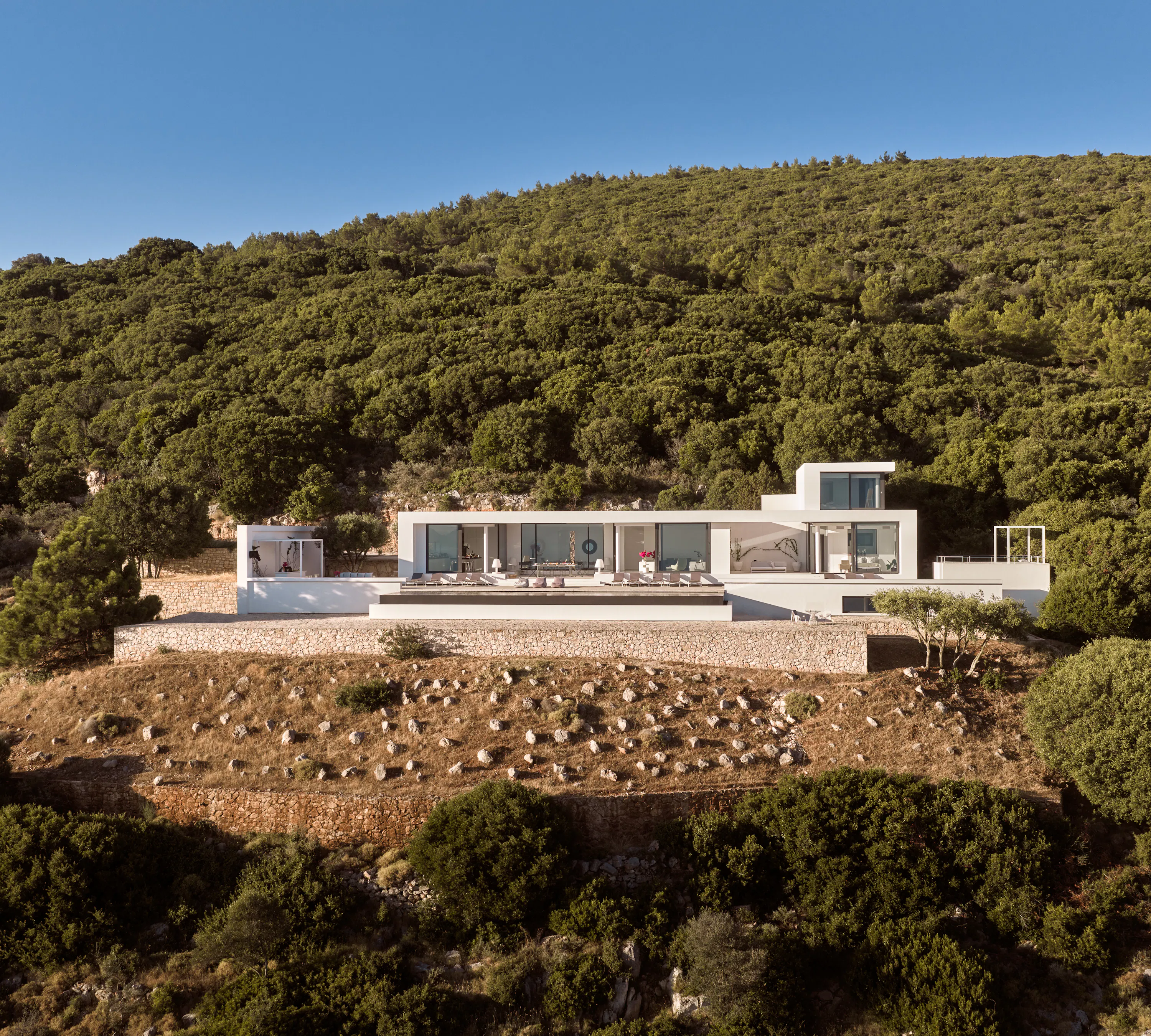 Aerial view of the villa surrounded by dense green hillside, showing the pool terrace and building layout