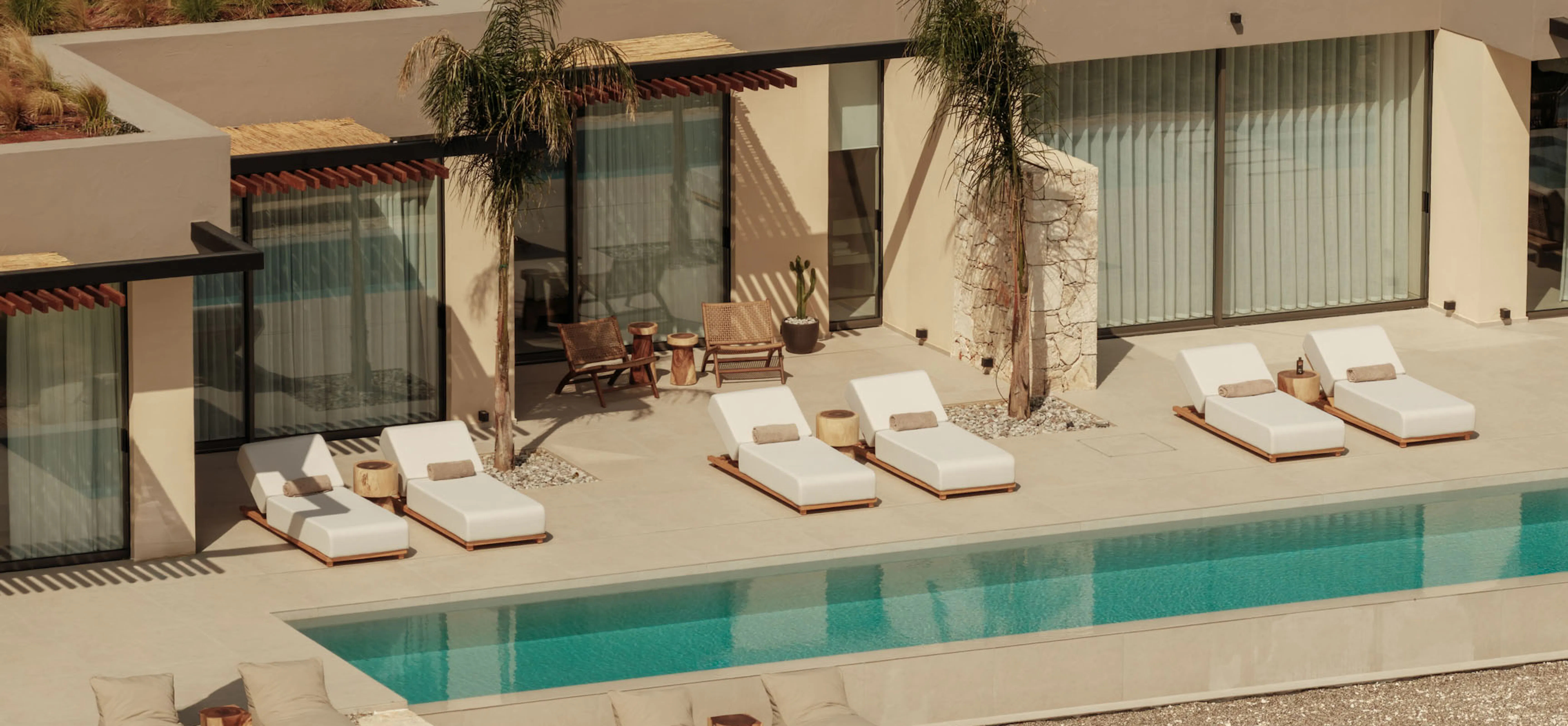 Aerial view of the villa's pool terrace with sun loungers, palm trees, and the surrounding hillside.