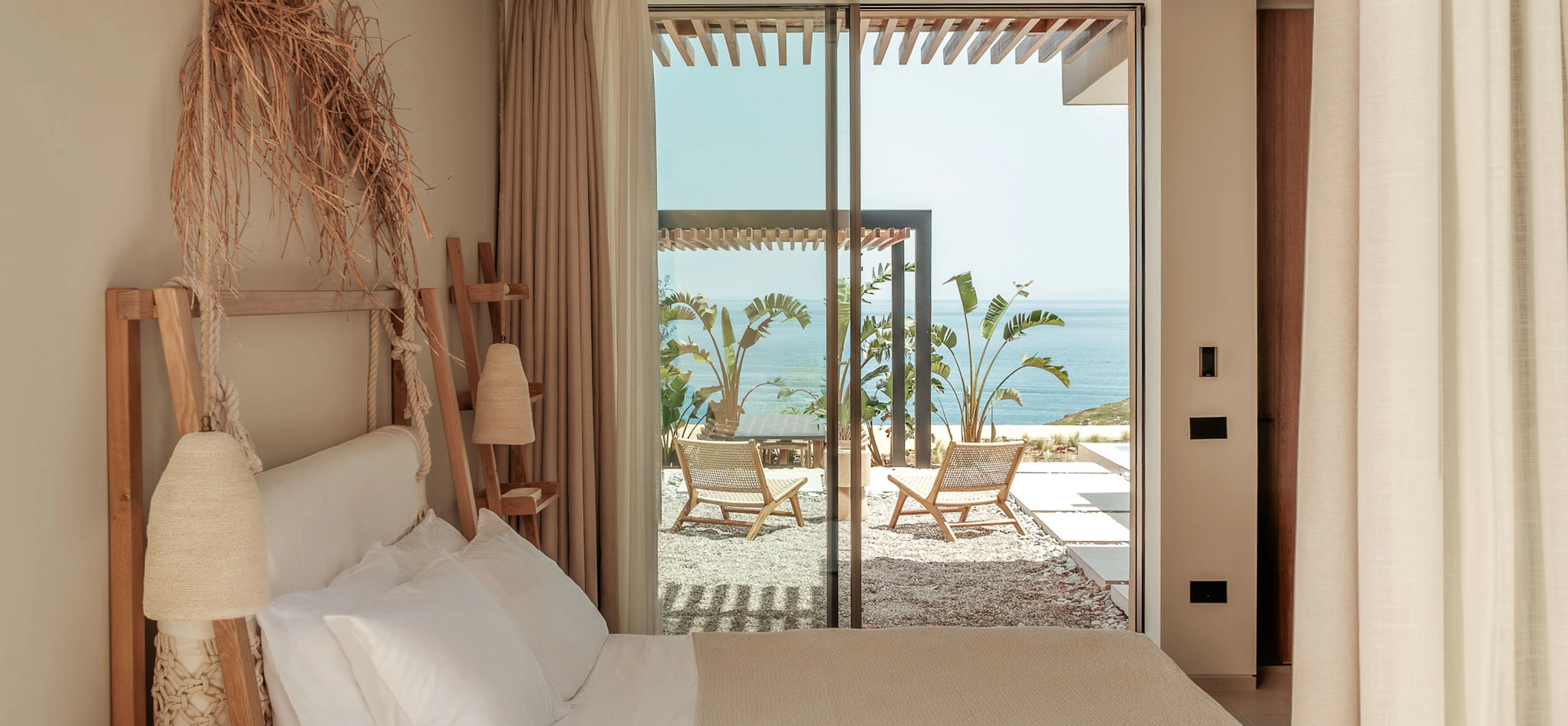 Bedroom with a rope-and-timber ladder headboard hung with dried grasses, a ceiling fan, and a sea view through the door.