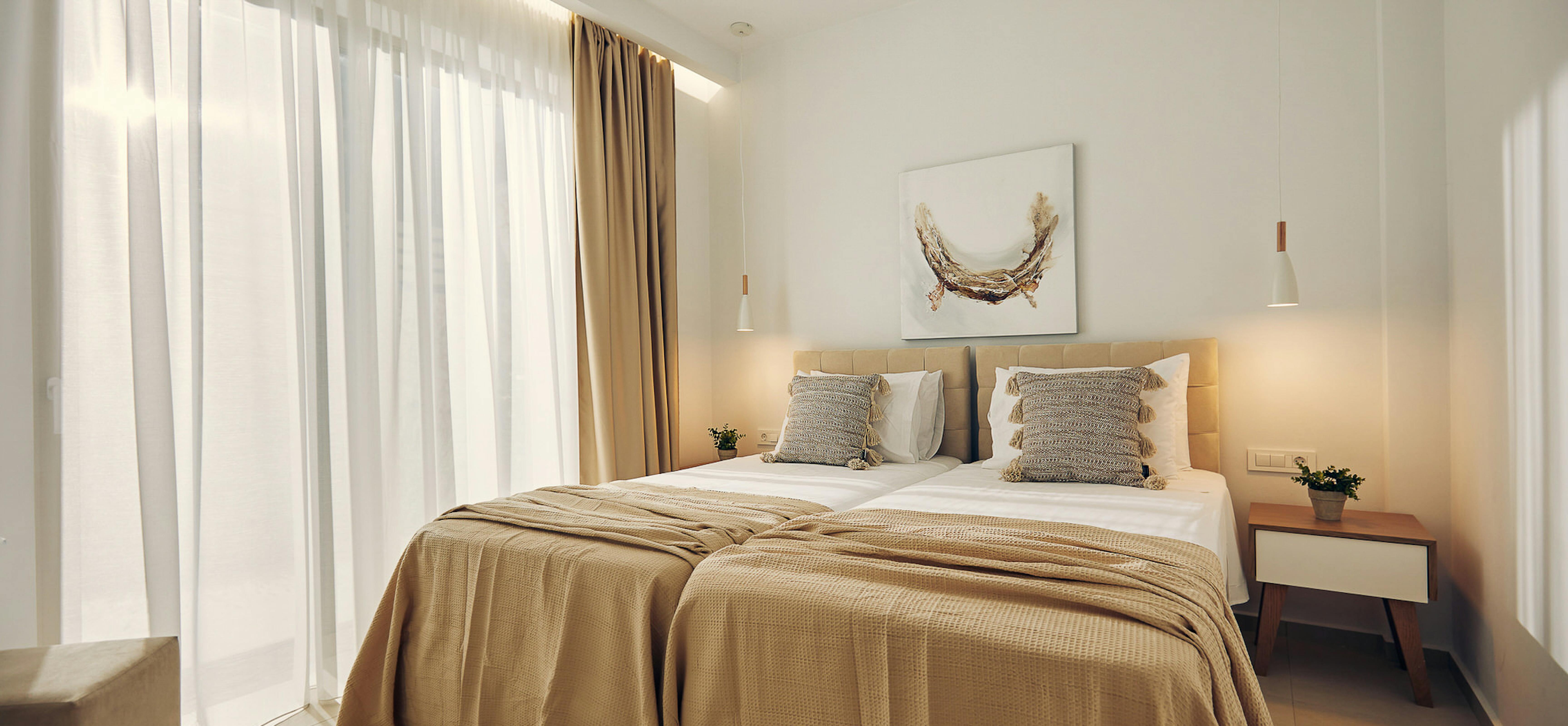 Bright bedroom with layered bedding, wall art depicting golden wreath, and sheer curtains filtering natural light.