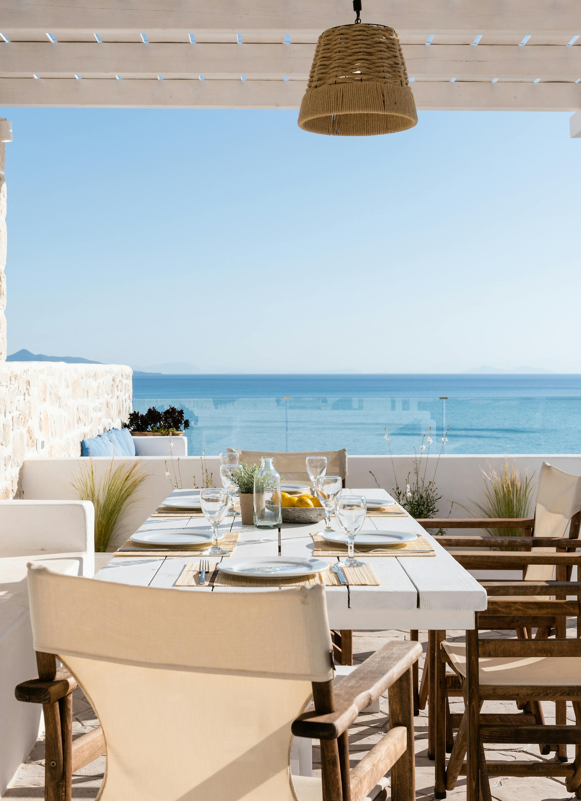 Covered dining terrace with set table, wooden director's chairs, and panoramic ocean views through pergola.