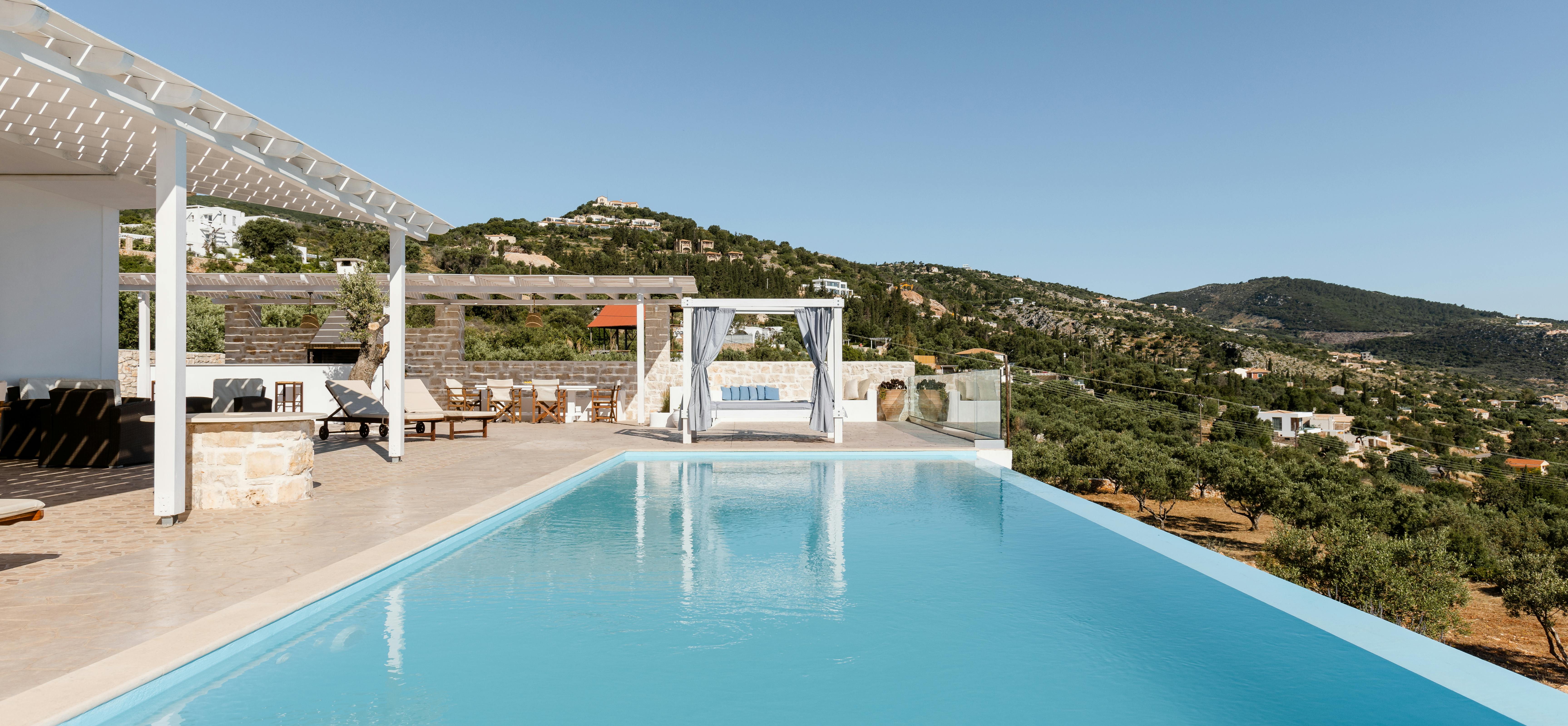 Infinity pool with turquoise water overlooking hillside landscape, featuring white pergola and canopied daybed.
