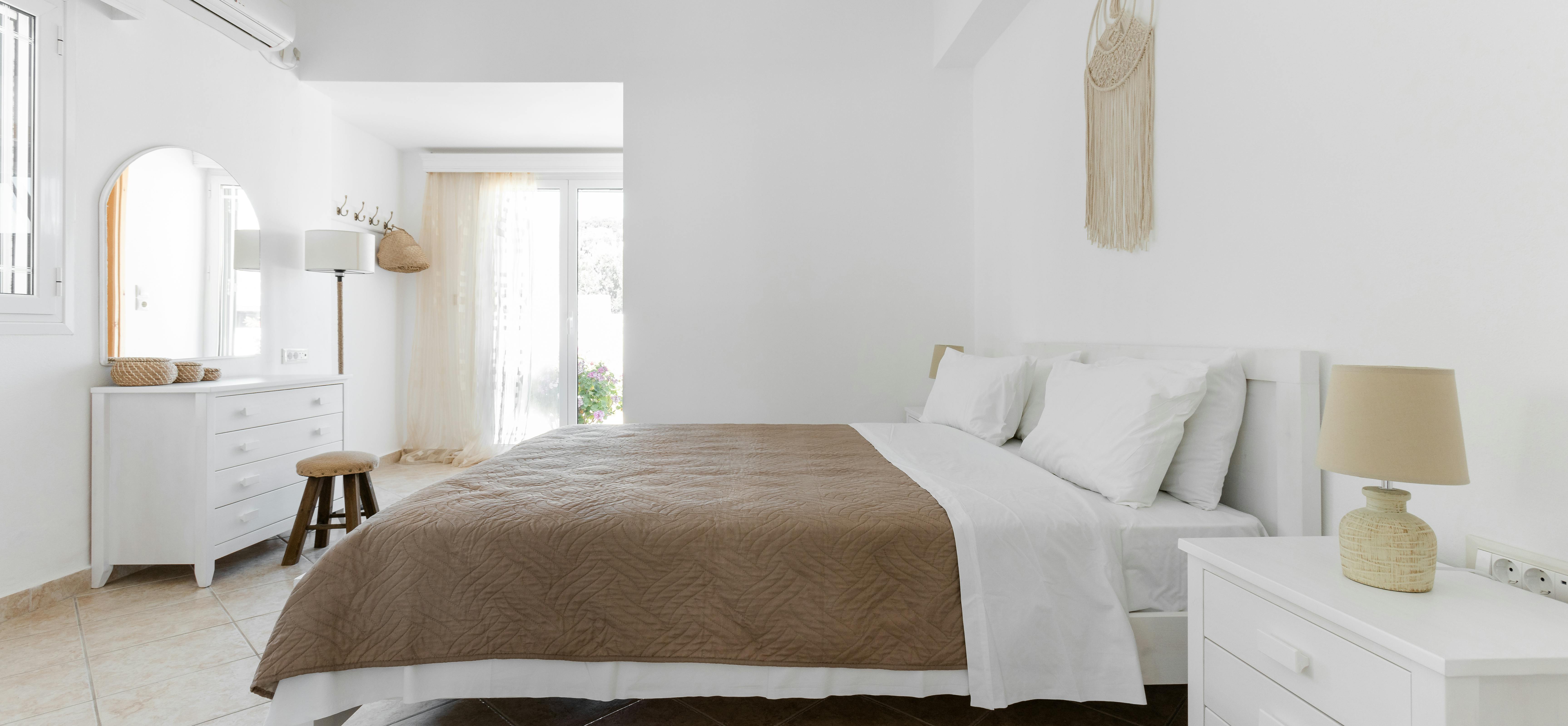 White minimalist bedroom with platform bed, dresser, arched doorway, and neutral taupe bedding.