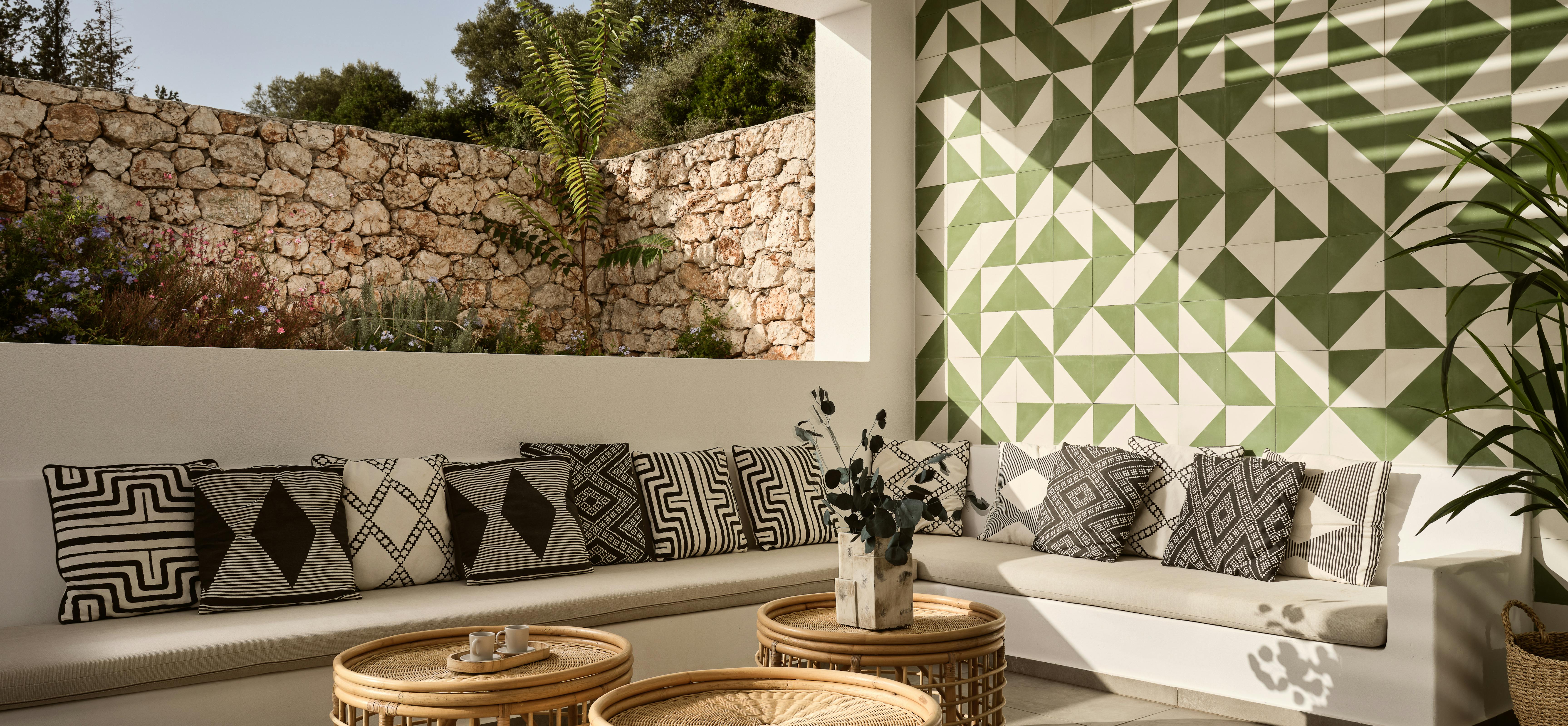 Covered outdoor lounge with built-in white benches, geometric cushions, green triangle tile accent wall, and woven coffee tables.