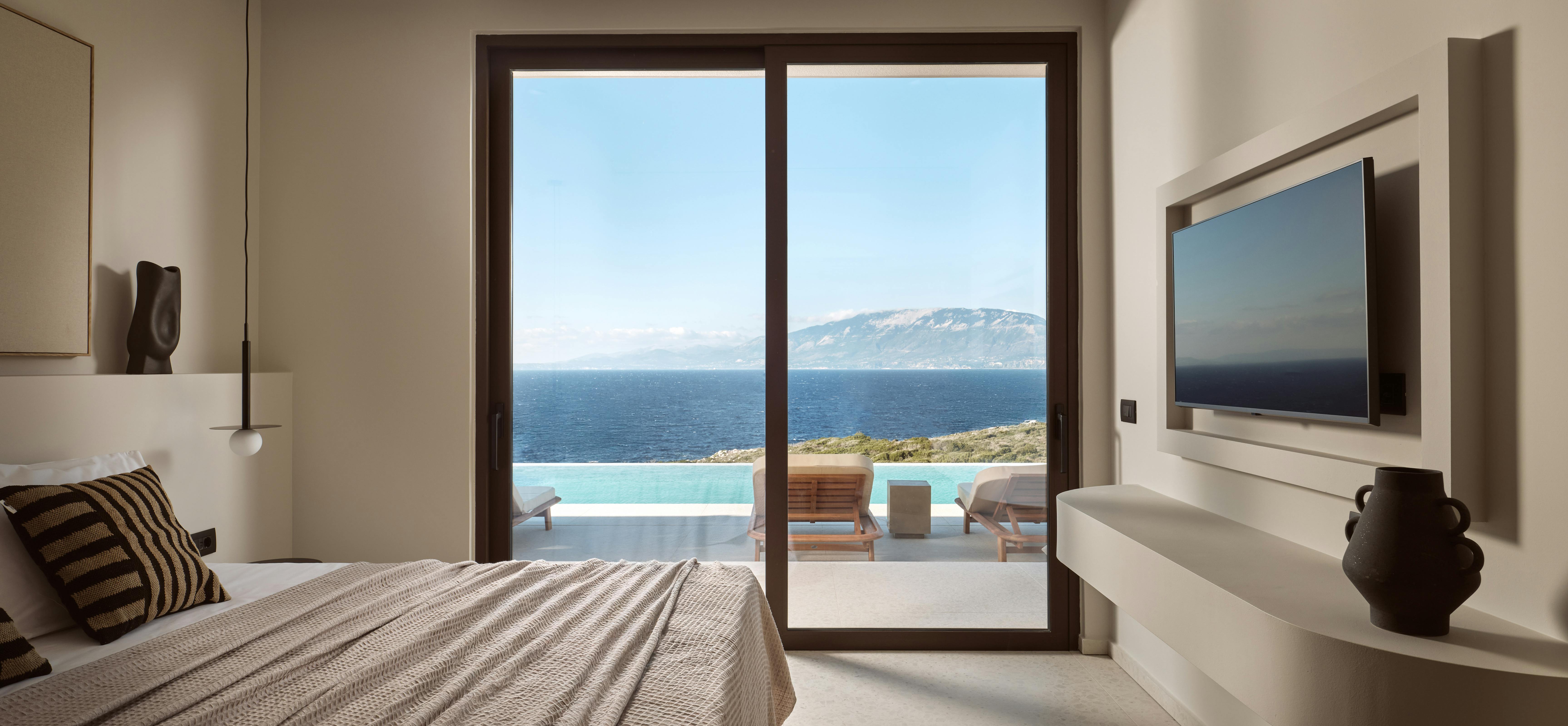 Luxurious bedroom with textured bedding, pendant light, and sliding glass doors opening to infinity pool terrace with dramatic ocean and mountain views.