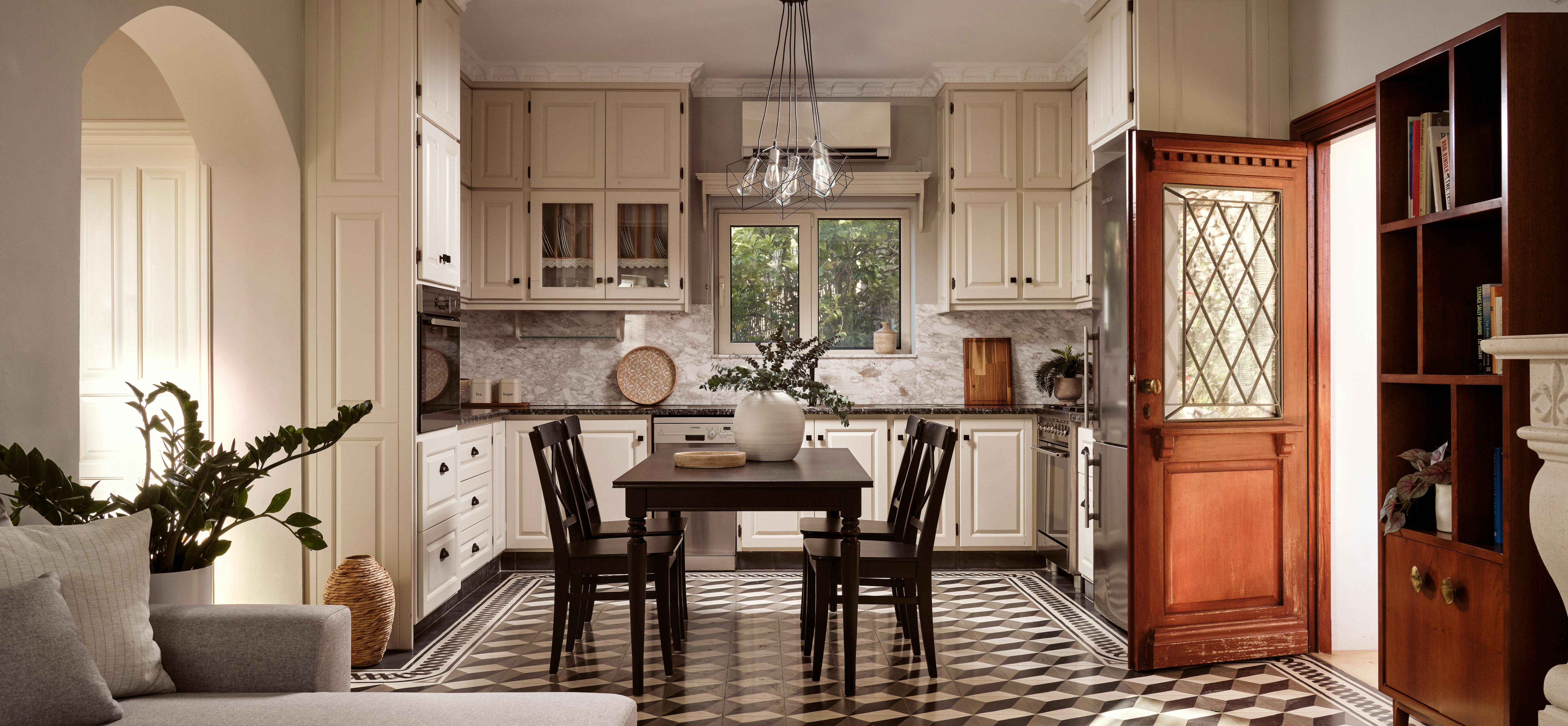 An open-plan kitchen and living area features cream cabinetry, geometric tile floors, and comfortable seating areas. The space combines traditional design elements with modern functionality, including pendant lighting and built-in storage.