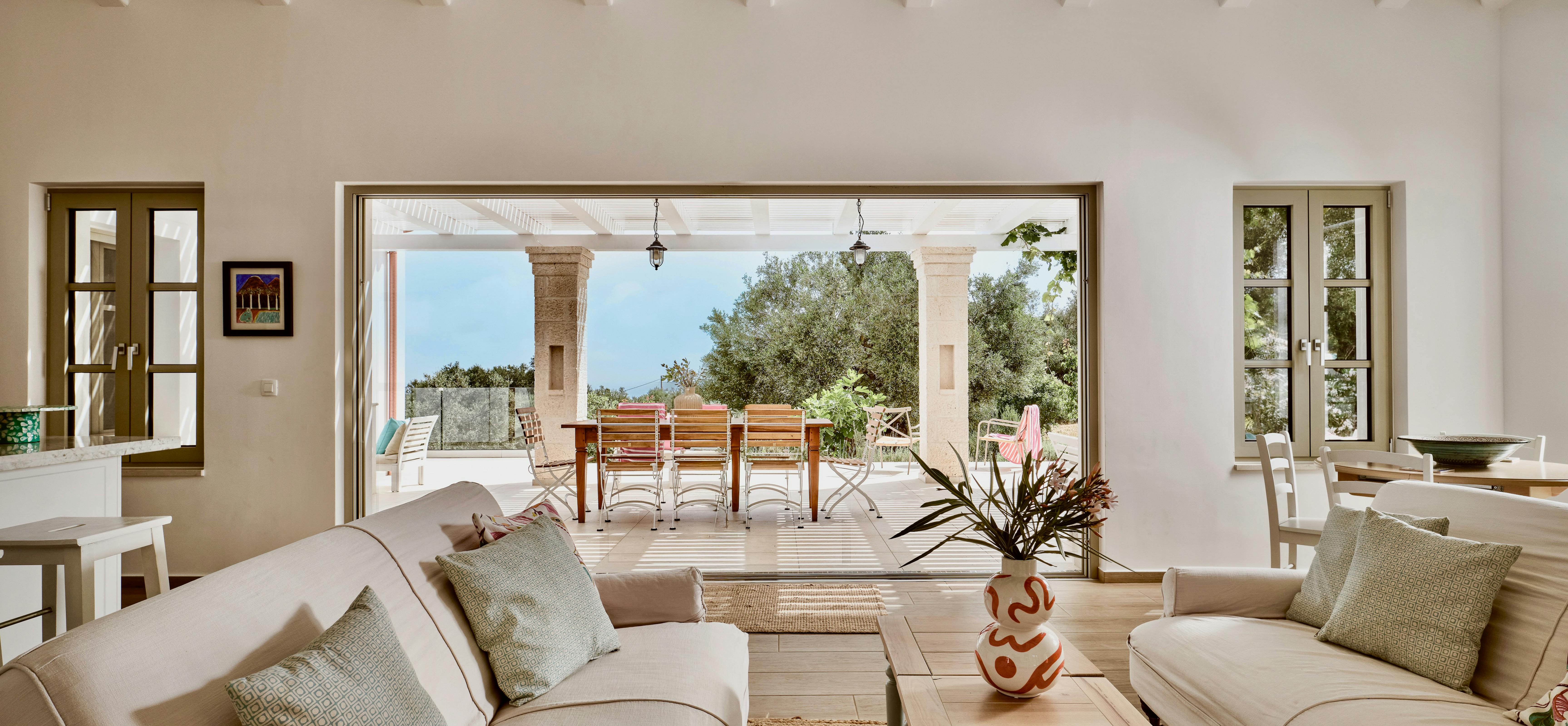 Main living area showing sectional seating arrangement facing the outdoor terrace. Exposed beams and large openings emphasise indoor-outdoor living.