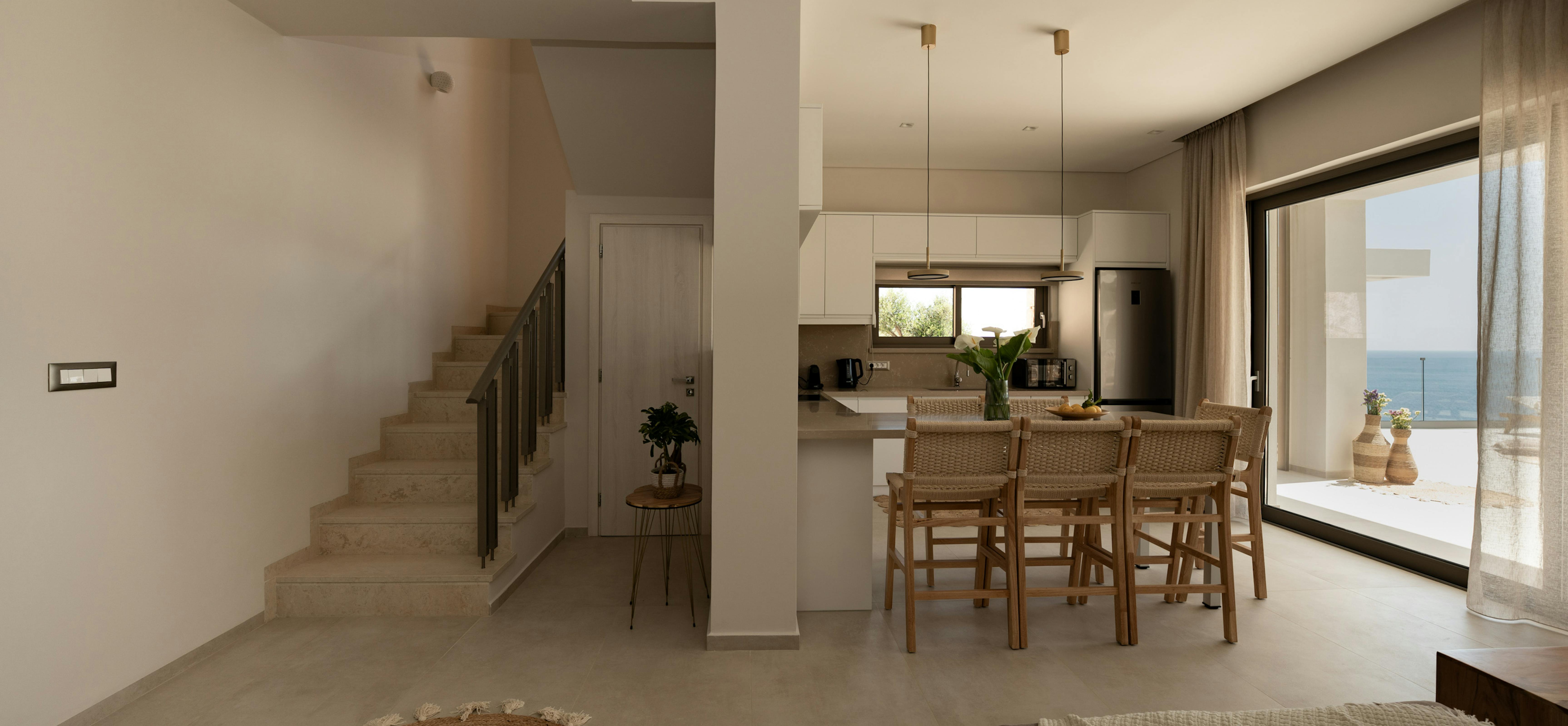 Open living space connecting kitchen, dining, and lounge areas with consistent neutral palette. Stone flooring and jute accents unify the multi-functional space.