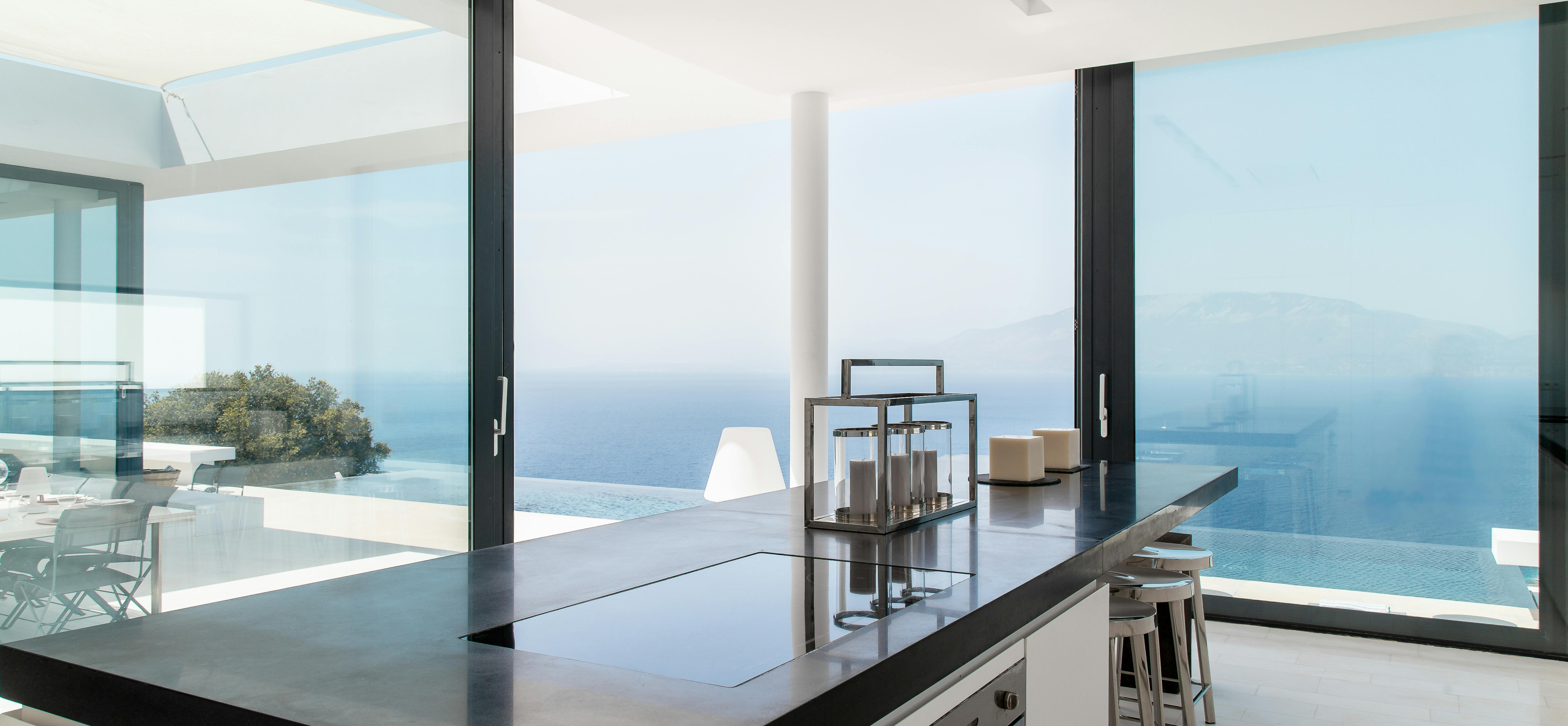 Contemporary kitchen with black countertops, white cabinetry, and floor-to-ceiling windows showcasing ocean views. Sleek design emphasises indoor-outdoor living with terrace access.