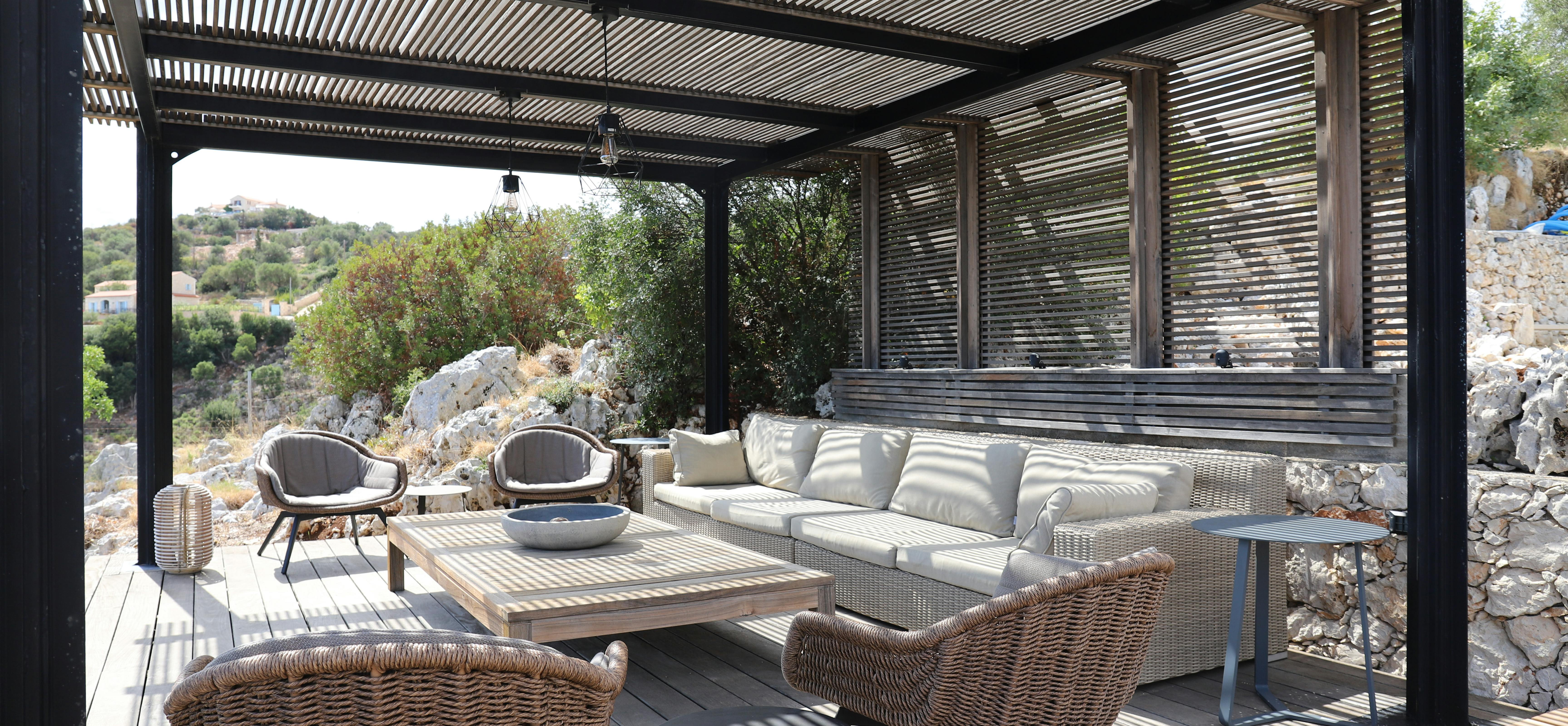 Covered outdoor living area with wicker furniture, slatted pergola roof, and stone wall details.