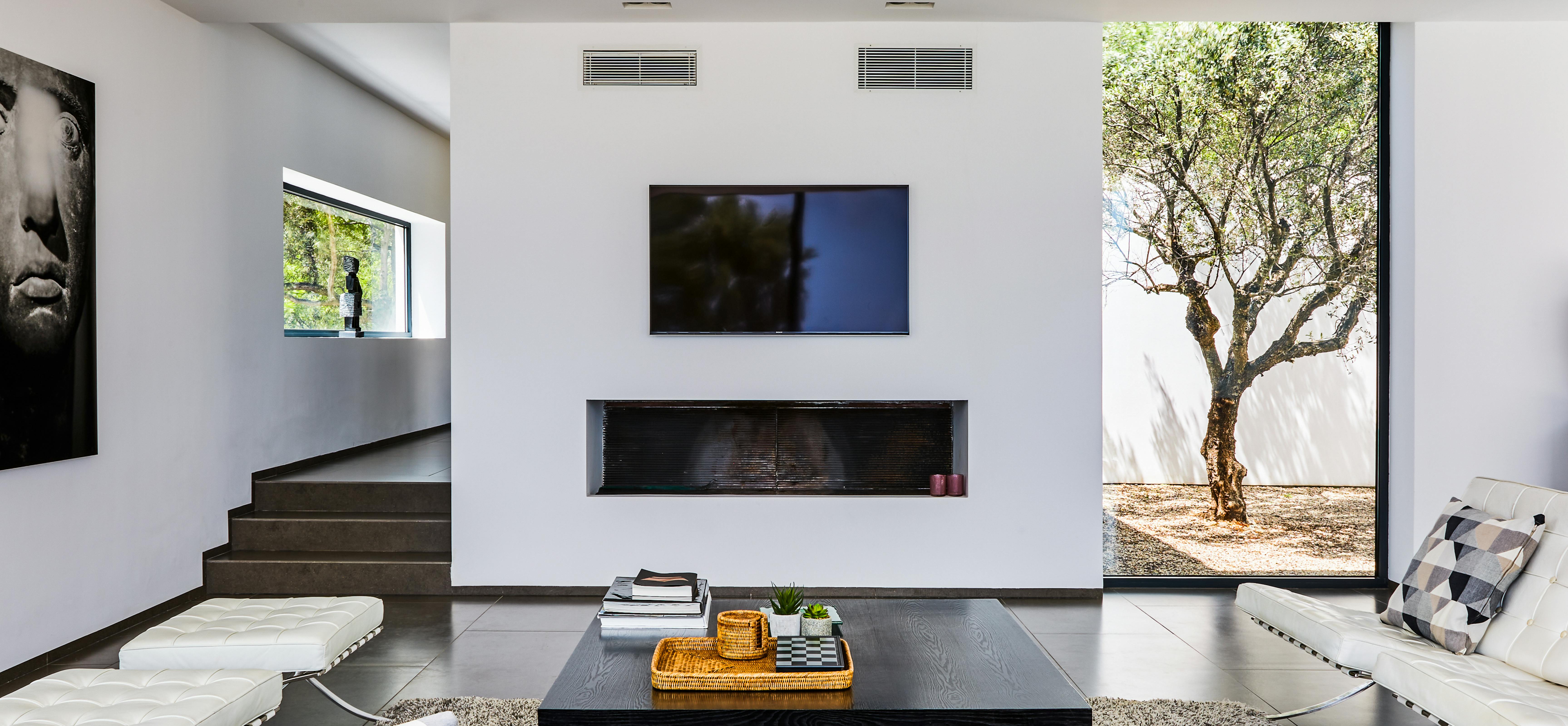 Contemporary living room with built-in fireplace, modern furniture, and courtyard tree view.