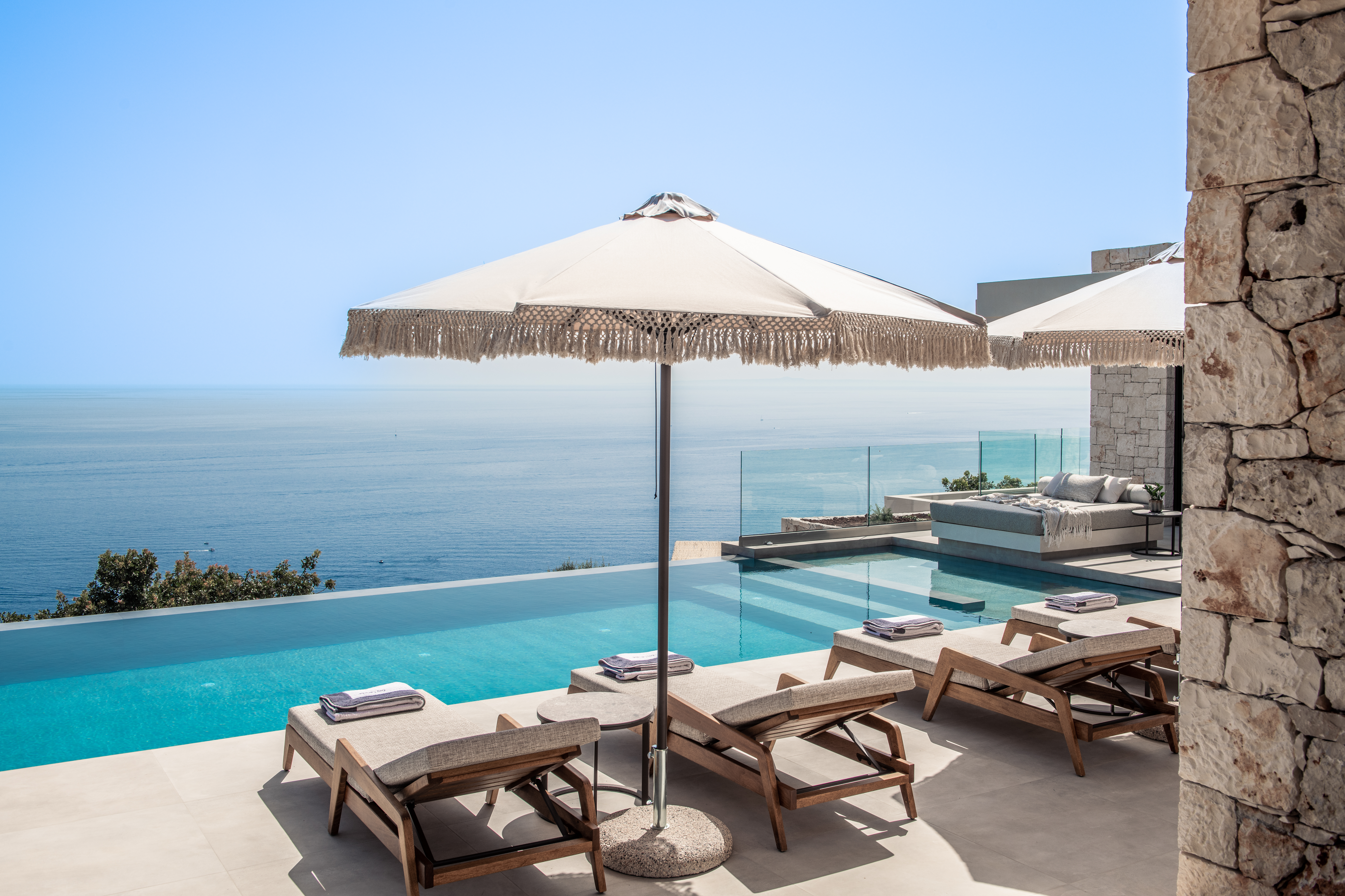 Infinity pool deck with wooden loungers, fringed umbrella, and dramatic ocean horizon views.