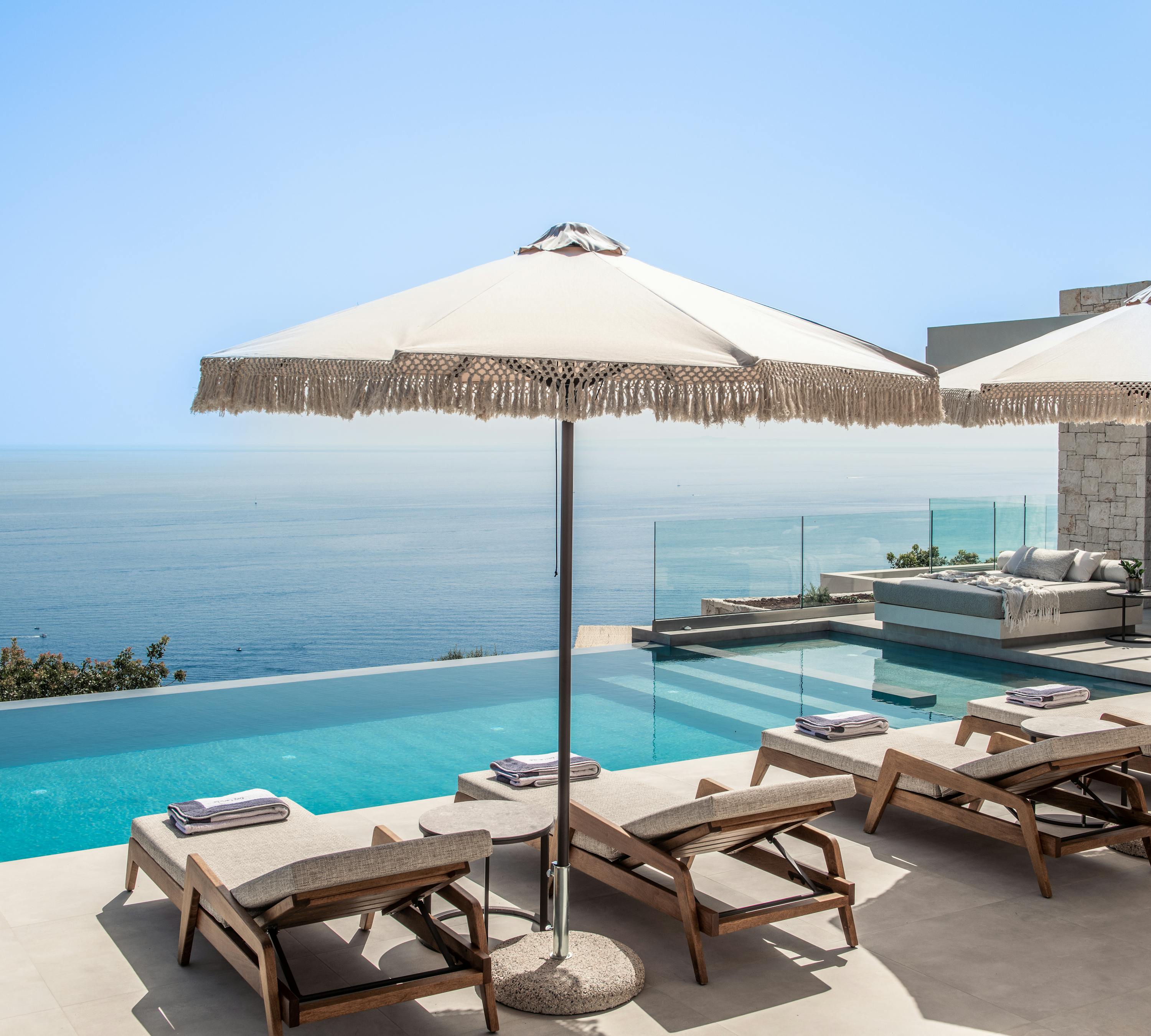 Infinity pool deck with wooden loungers, fringed umbrella, and dramatic ocean horizon views.