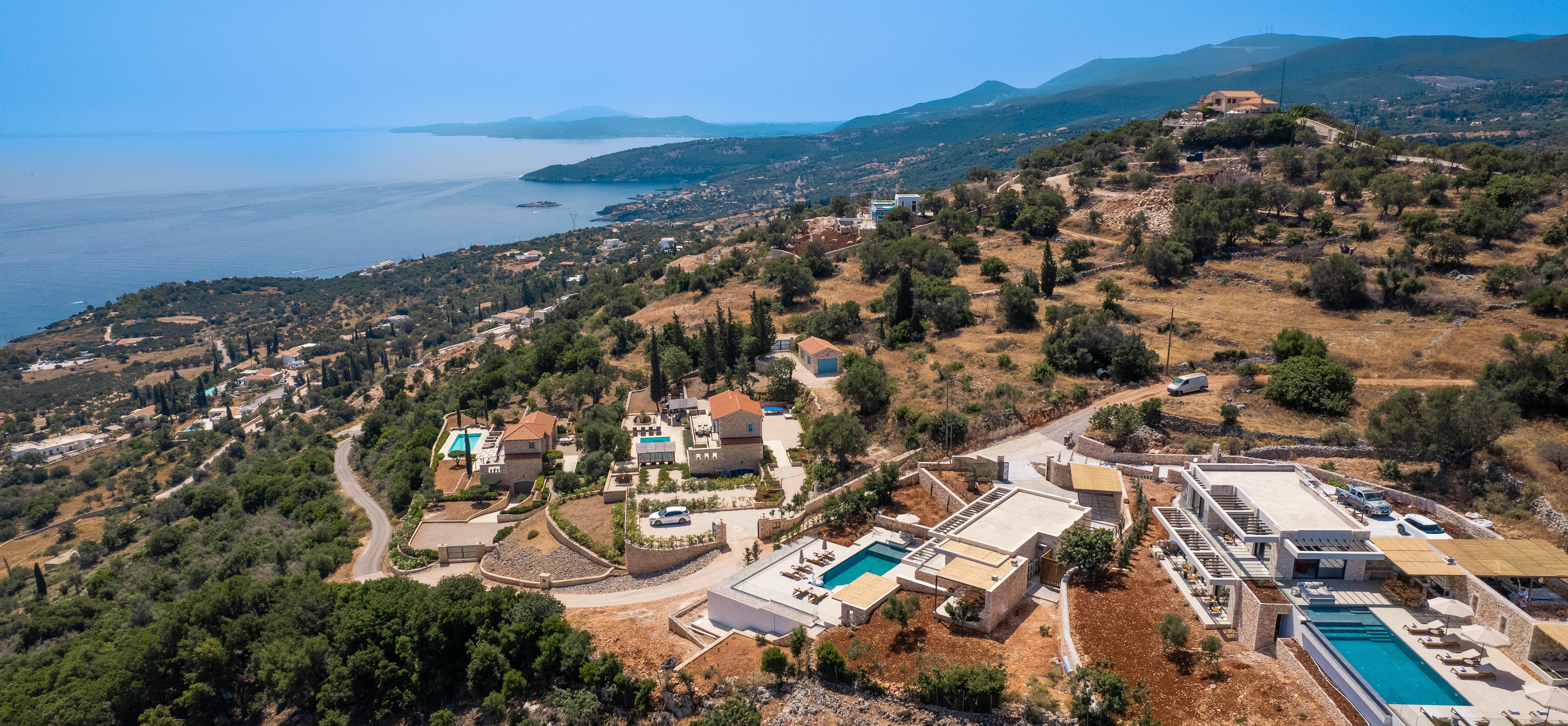 Aerial view of Mediterranean coastal development with luxury villas, pools, and forested hillsides.