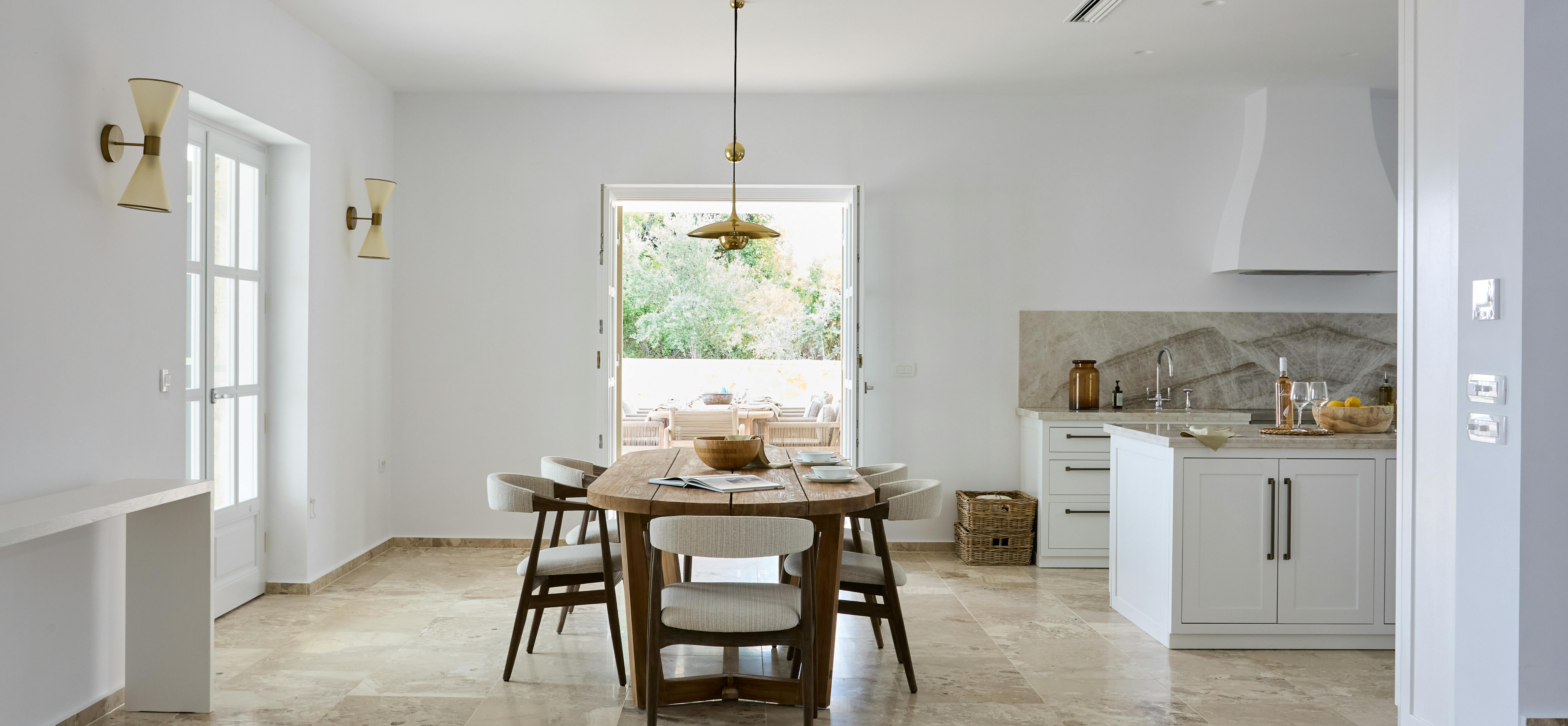The kitchen combines white cabinetry with natural stone bench tops and a dramatic veined marble splash back. Brass pendant lighting and timber dining furniture add warmth to the contemporary design.