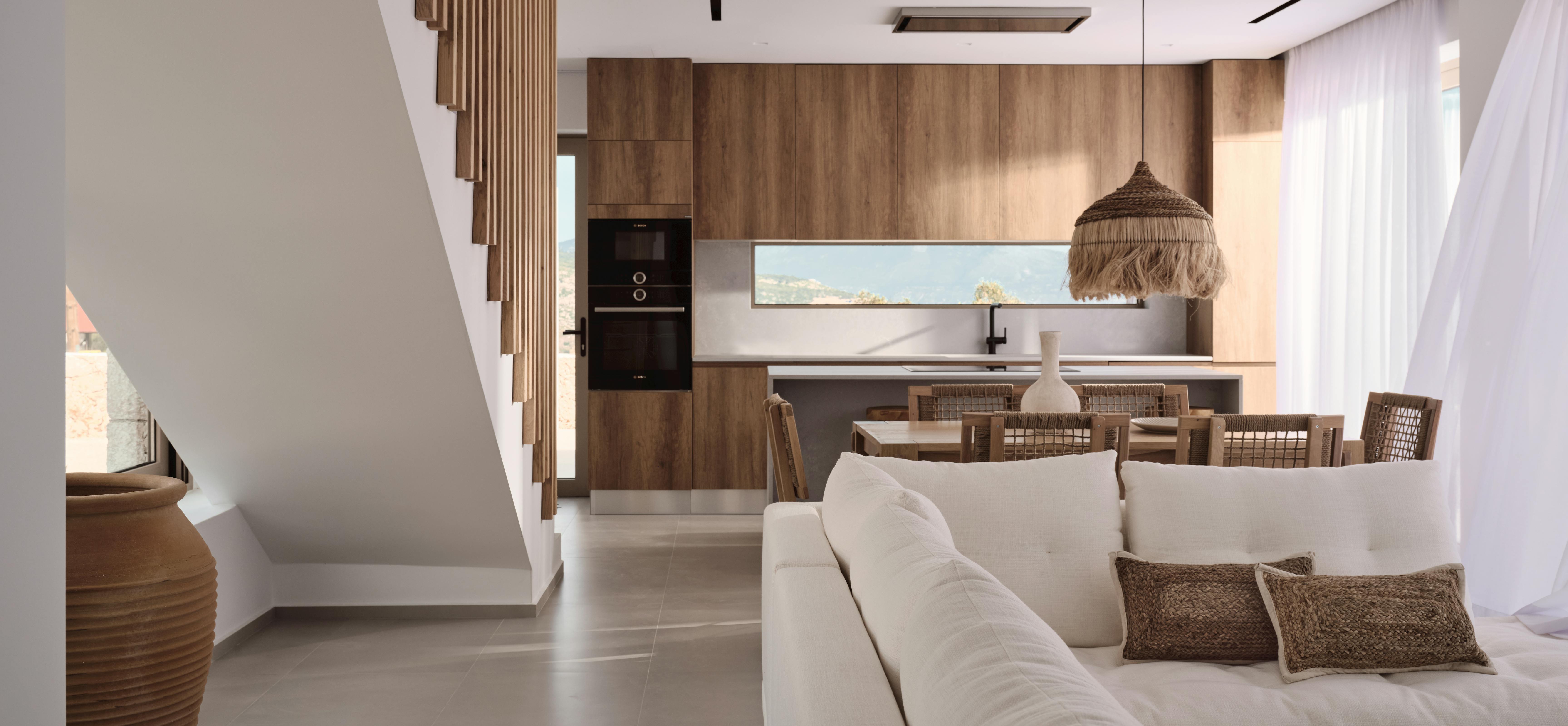 Open-plan living space with wooden staircase, modern kitchen, white sofa, and woven pendant lighting.