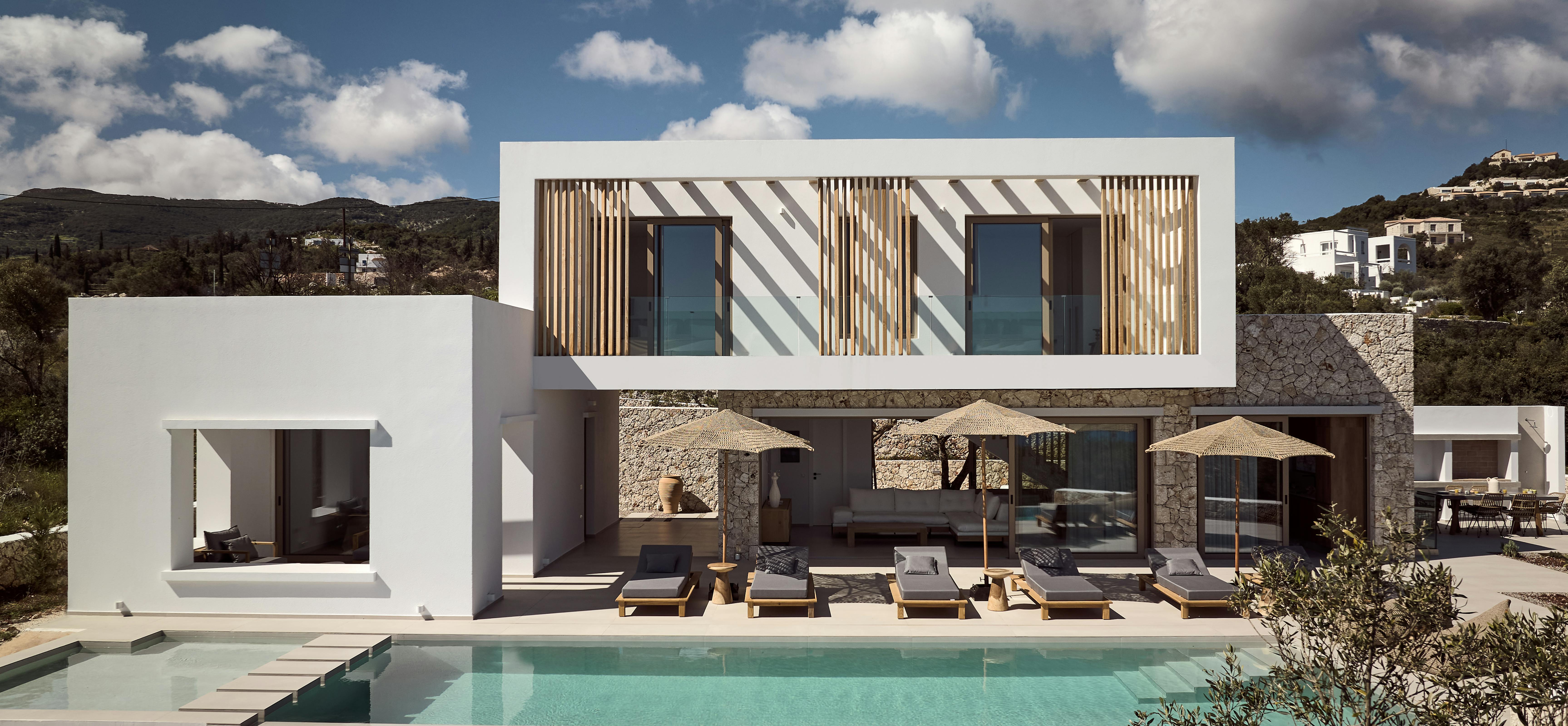 Modern two-story villa with wooden shutters, infinity pool, and dramatic hillside Mediterranean setting.