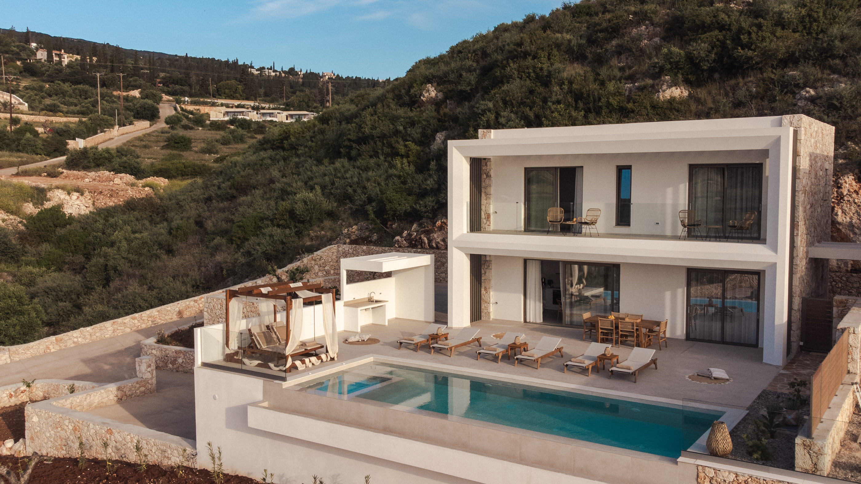 Modern white villa with swimming pool overlooking hillside landscape in Mediterranean setting.