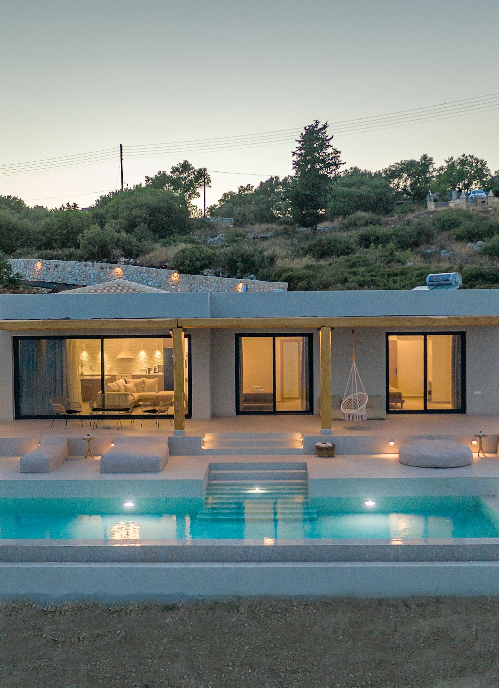 Contemporary hillside villa at twilight with illuminated infinity pool and minimalist lounging terrace.