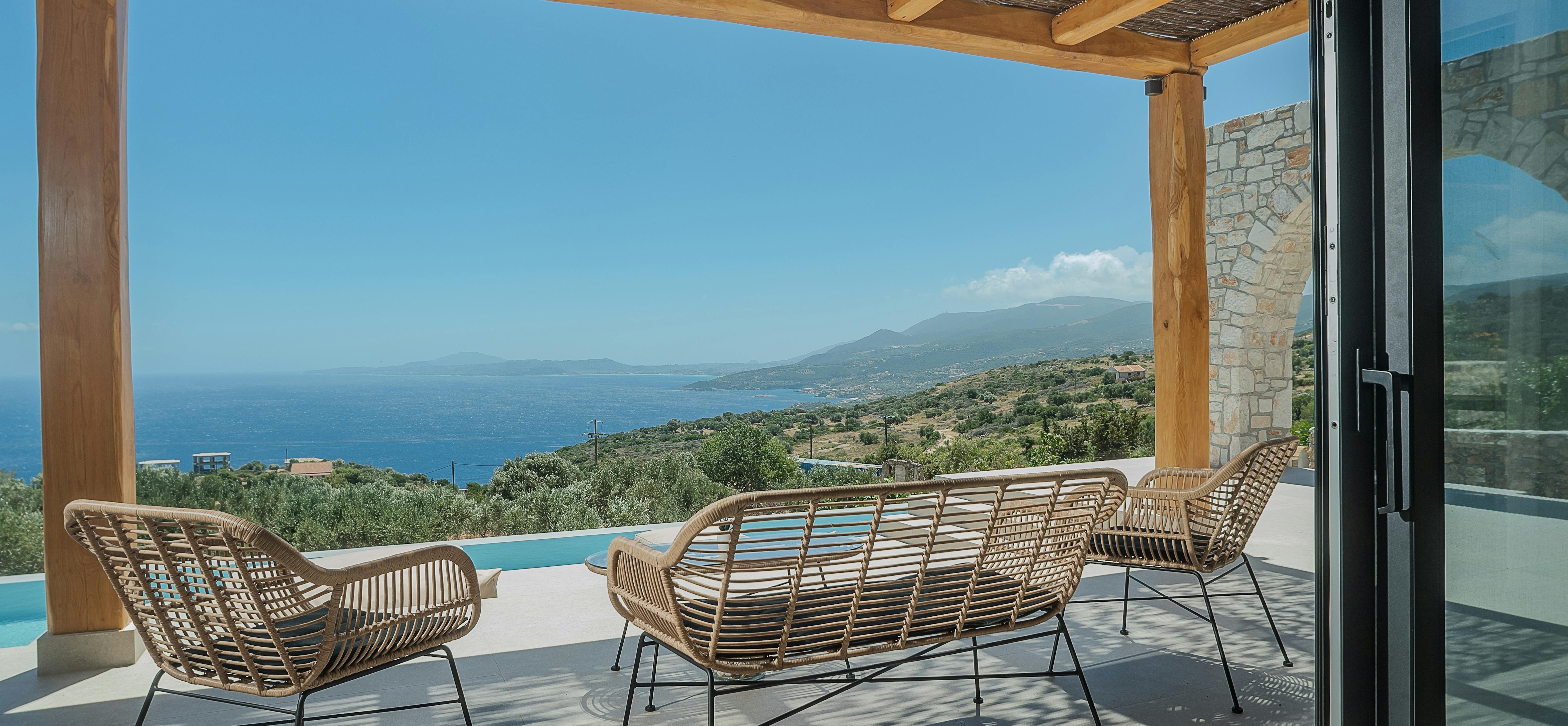 Covered terrace with rattan lounge chairs overlooking infinity pool and distant coastal views.