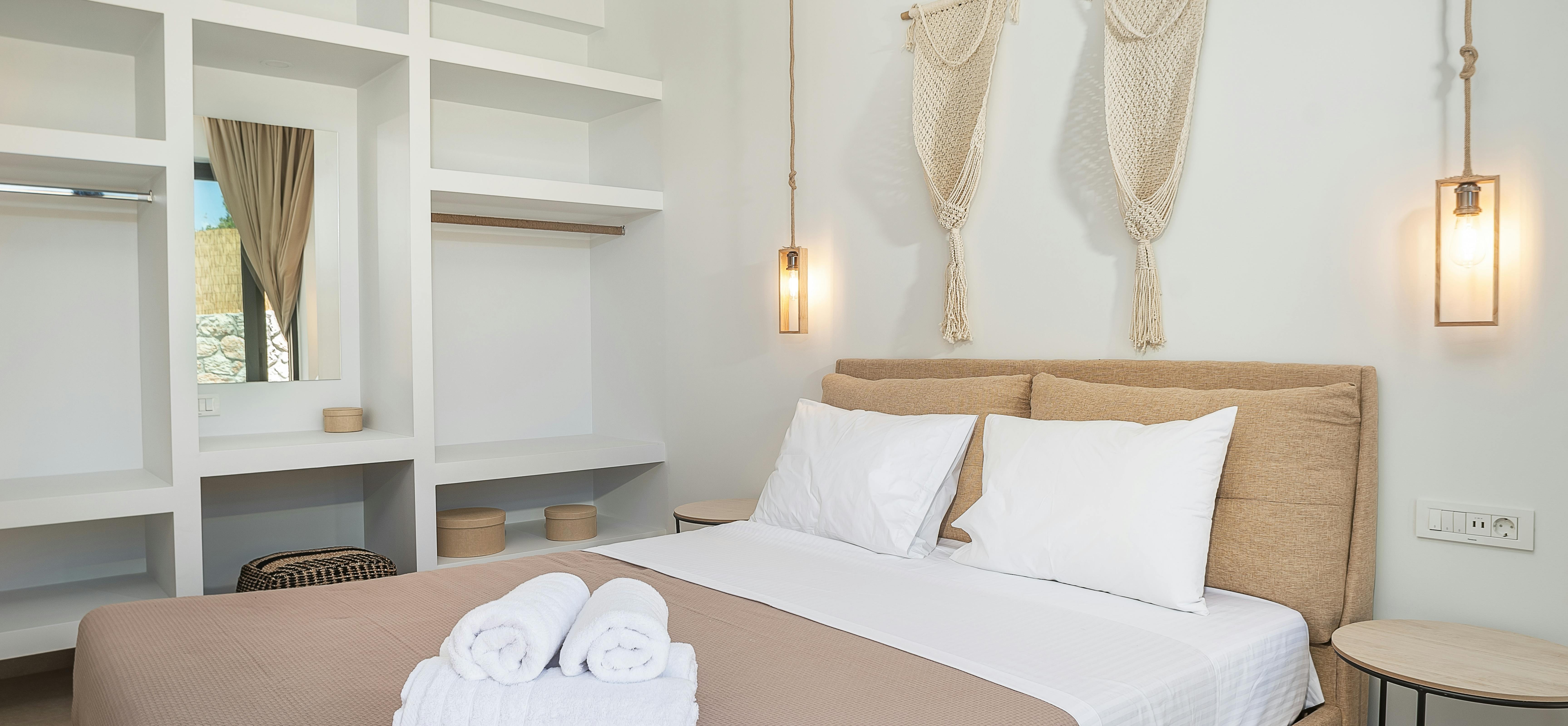 White bedroom with upholstered headboard, macramé wall hangings, and built-in shelving niches.