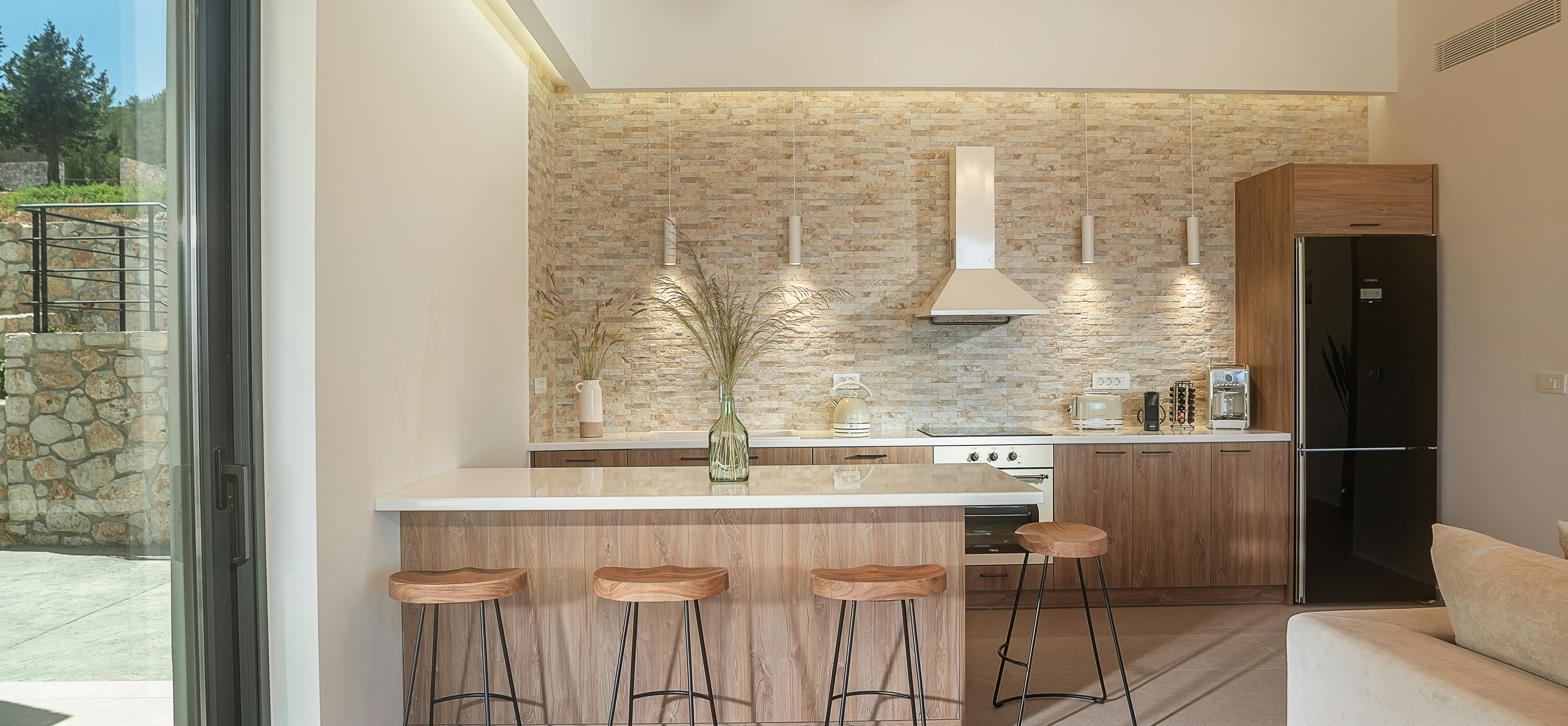Open-plan kitchen with breakfast bar, wooden stools, and stone feature wall under exposed beams.
