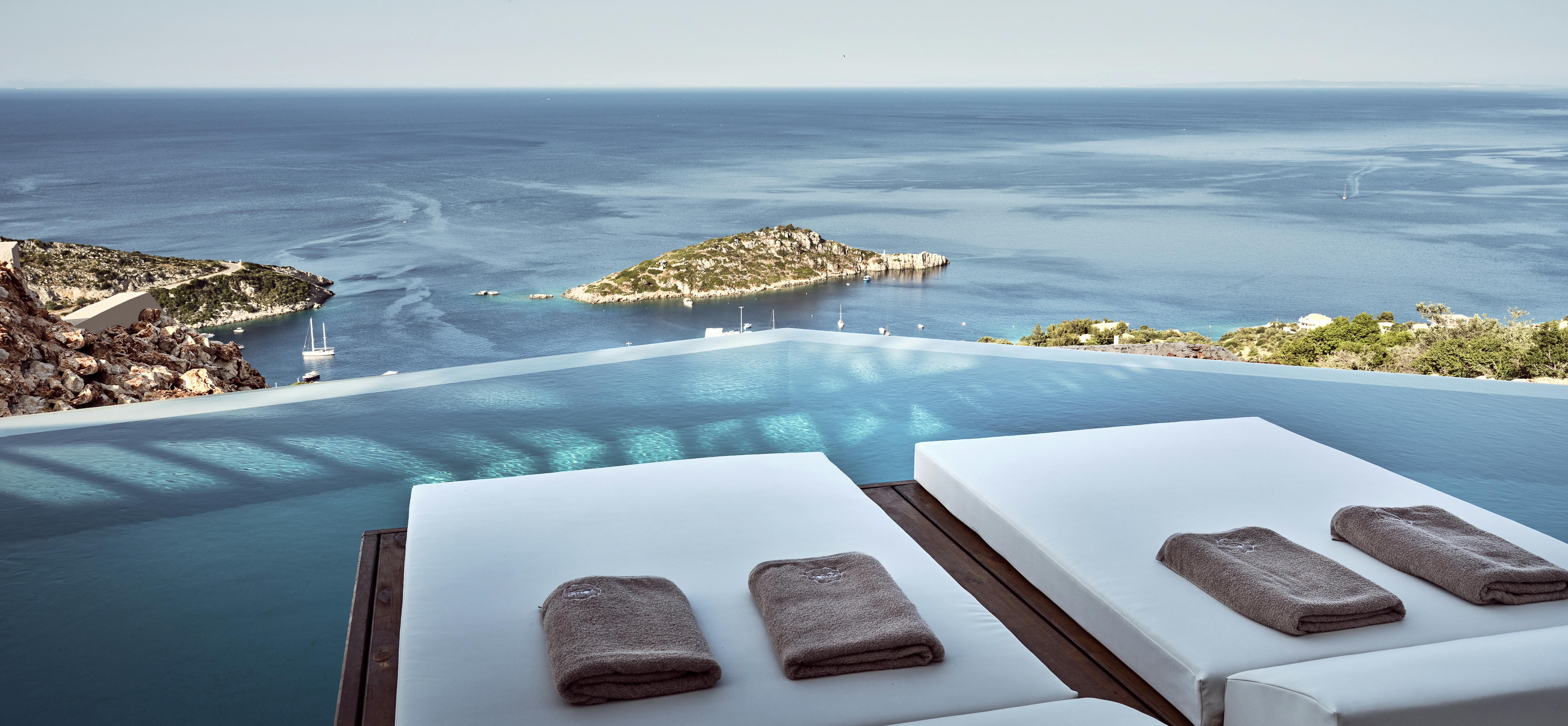 Two white pool loungers with rolled towels facing infinity edge and distant island.