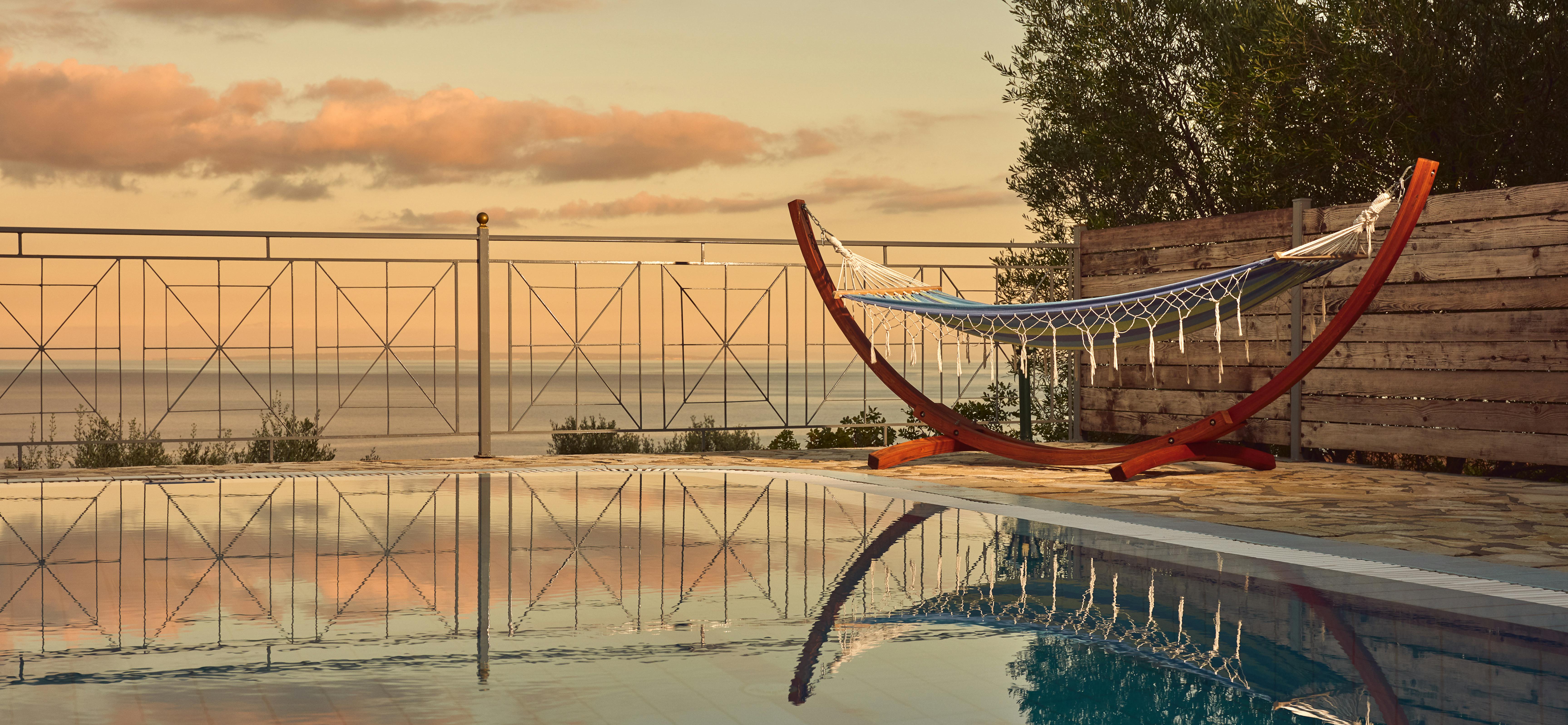 Serene pool reflection at golden hour with hammock and Mediterranean coastal backdrop.