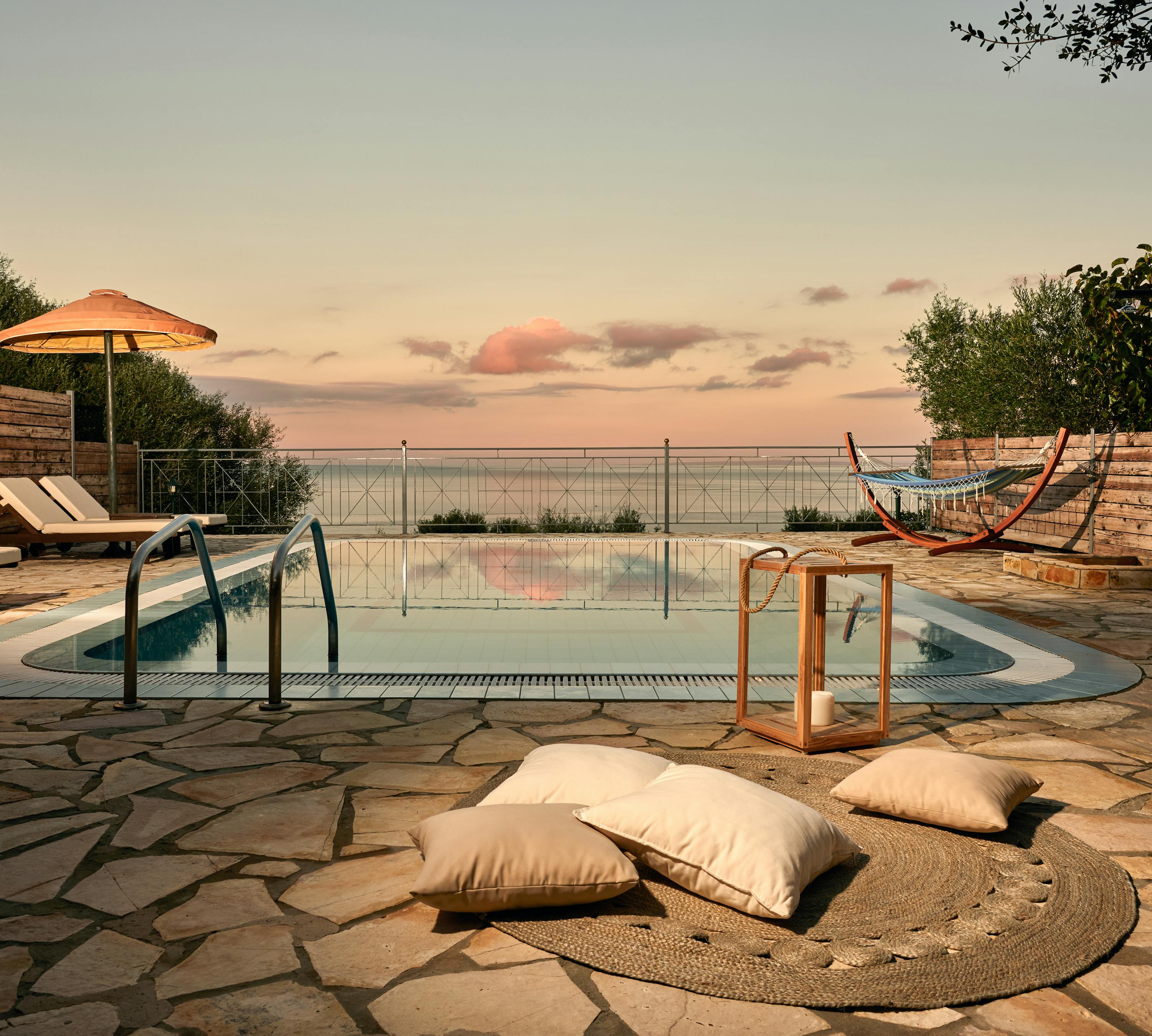 Peaceful pool setting at sunset with hammock and natural stone paving reflecting in still water.
