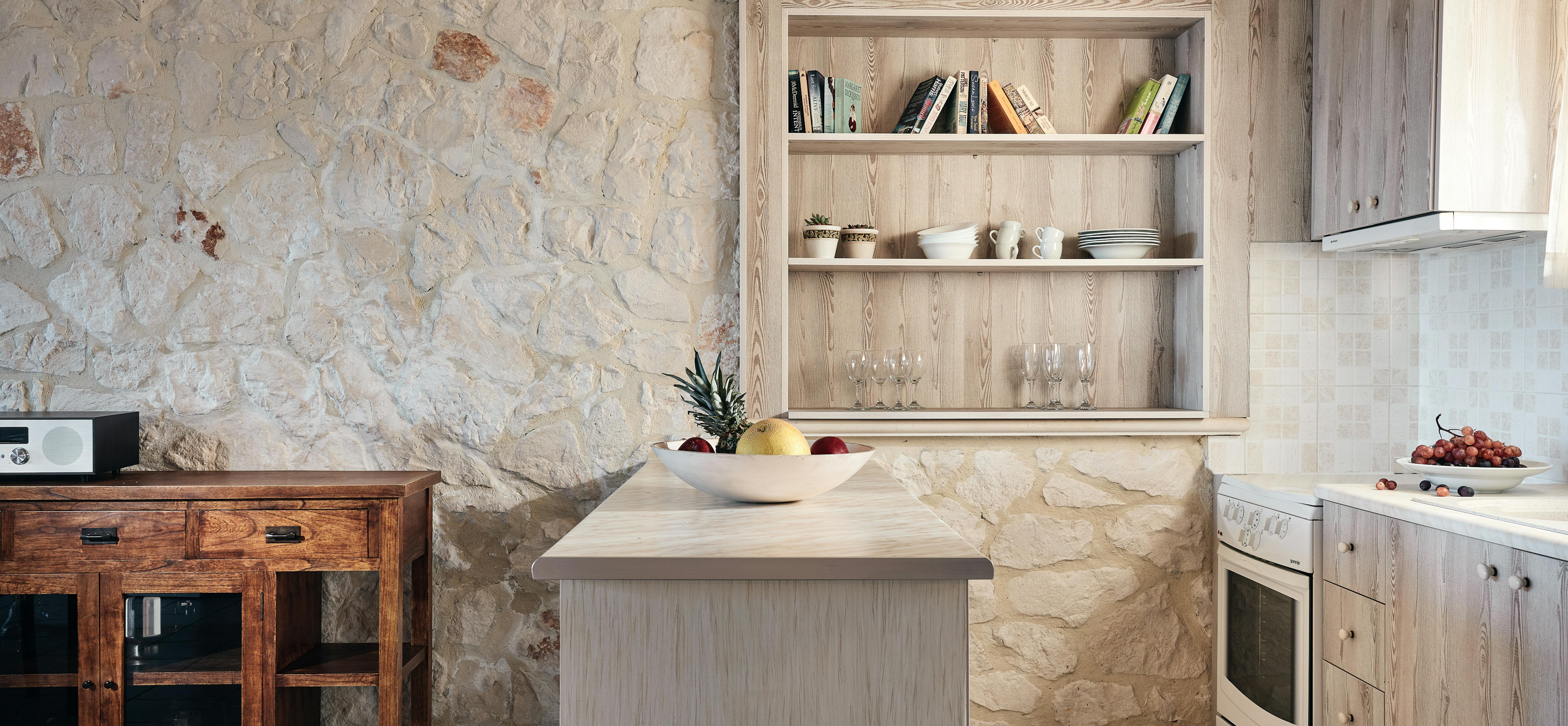 Rustic kitchen with exposed stone walls, wooden cabinetry, and built-in display shelving.