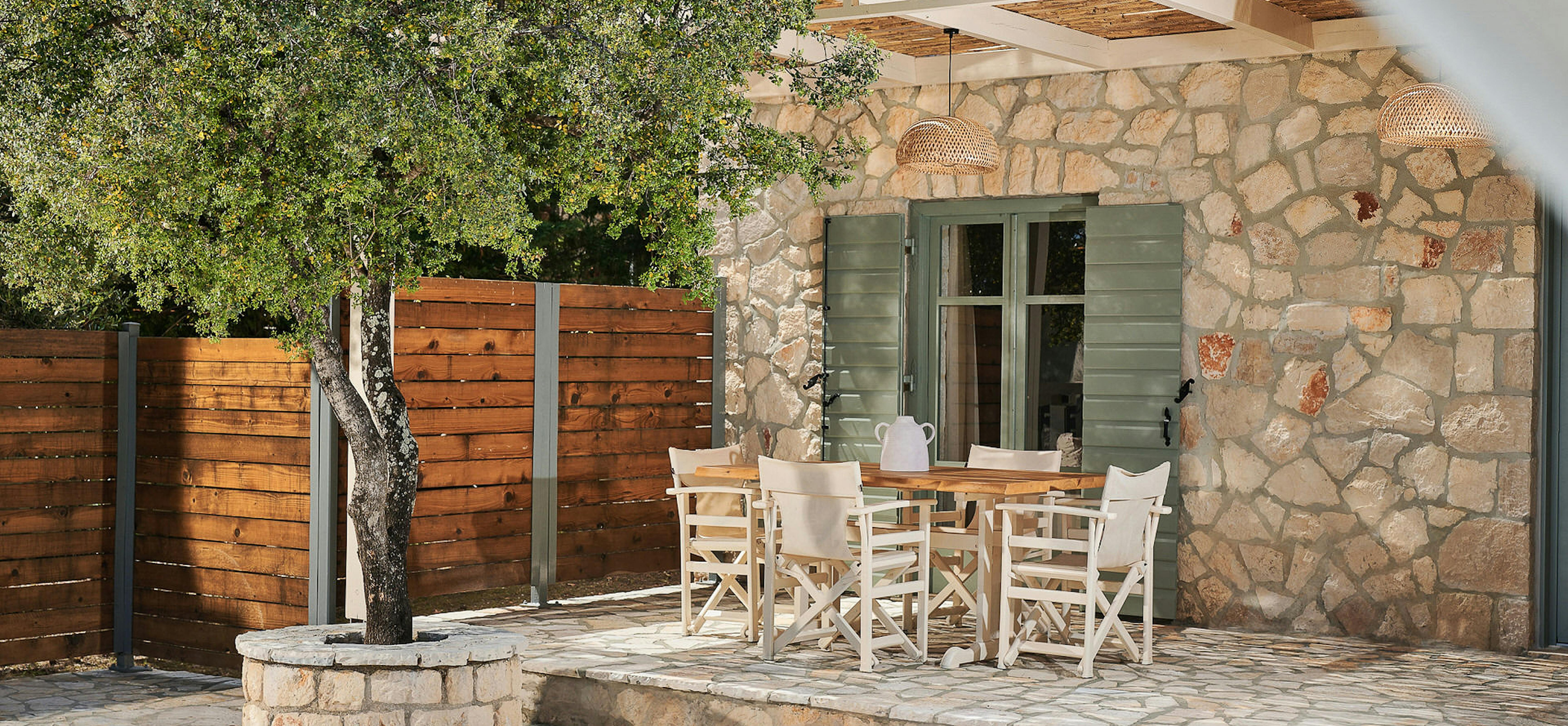 Outdoor dining terrace with white director's chairs and rustic stone architecture.