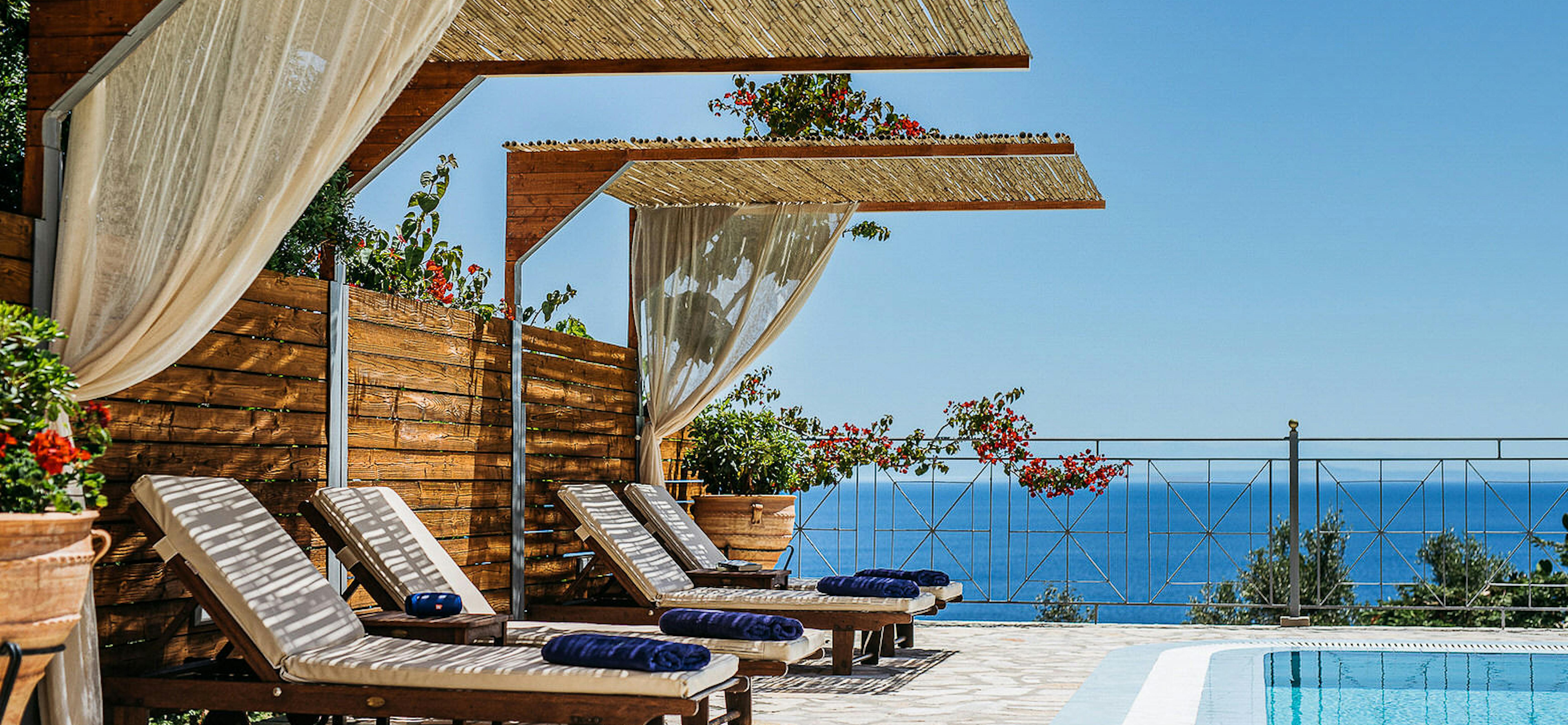 Pool area with wooden shade canopies and loungers overlooking blue ocean waters.