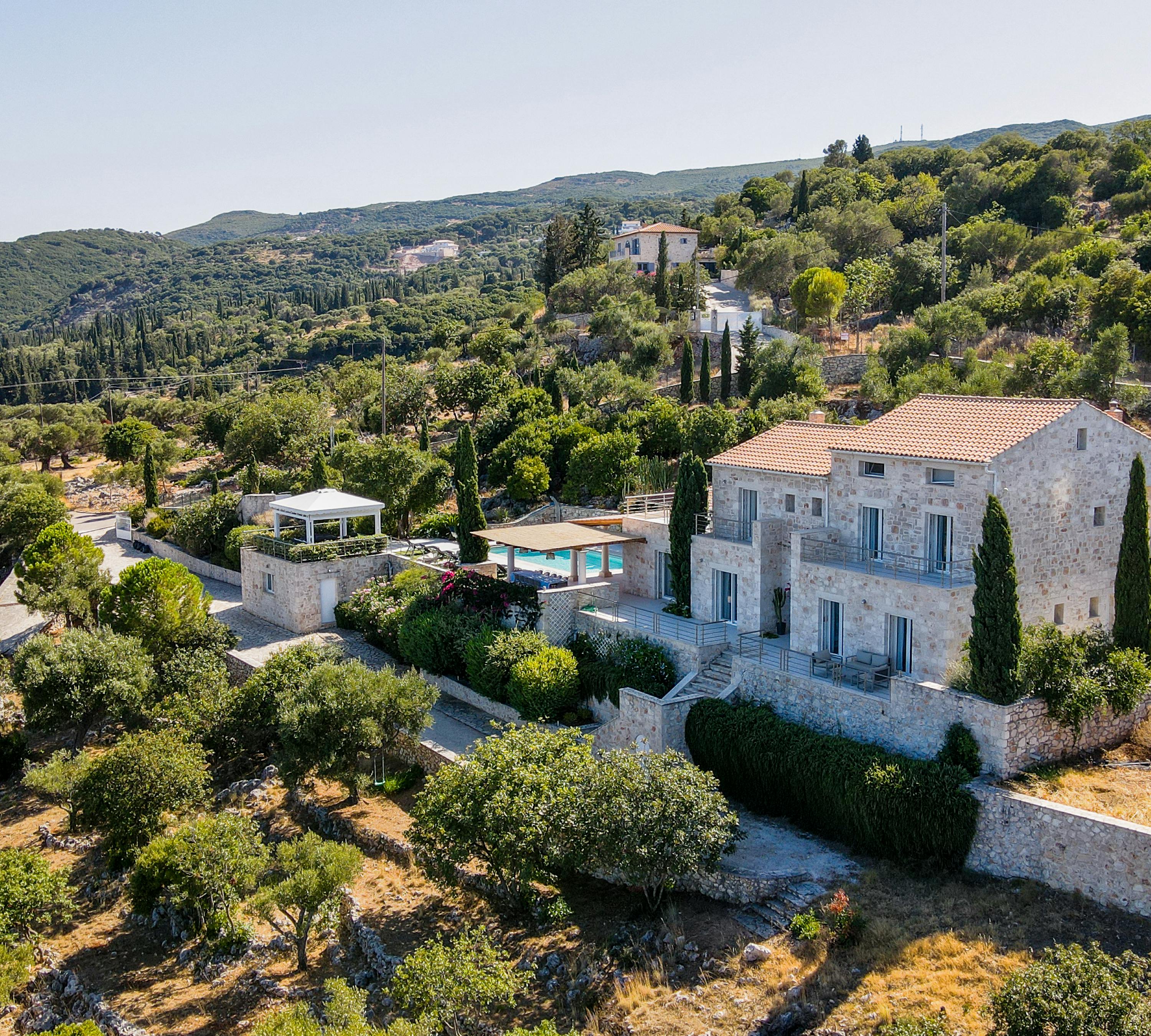 Aerial view of Mediterranean stone villa with terracotta roofs nestled in lush hillside landscape.