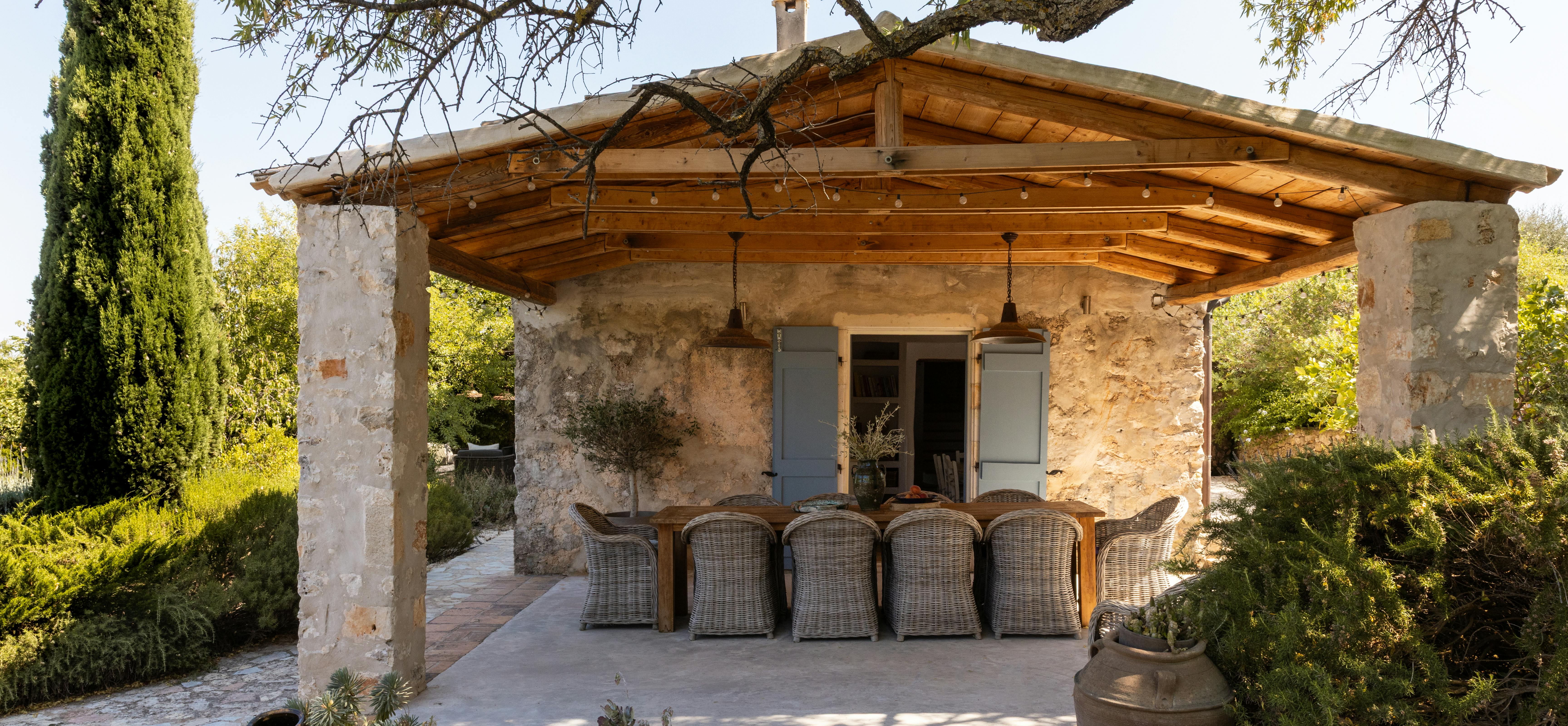 Outdoor dining pergola with rustic stone walls, woven chairs, and ancient olive tree providing natural shade over terrace.