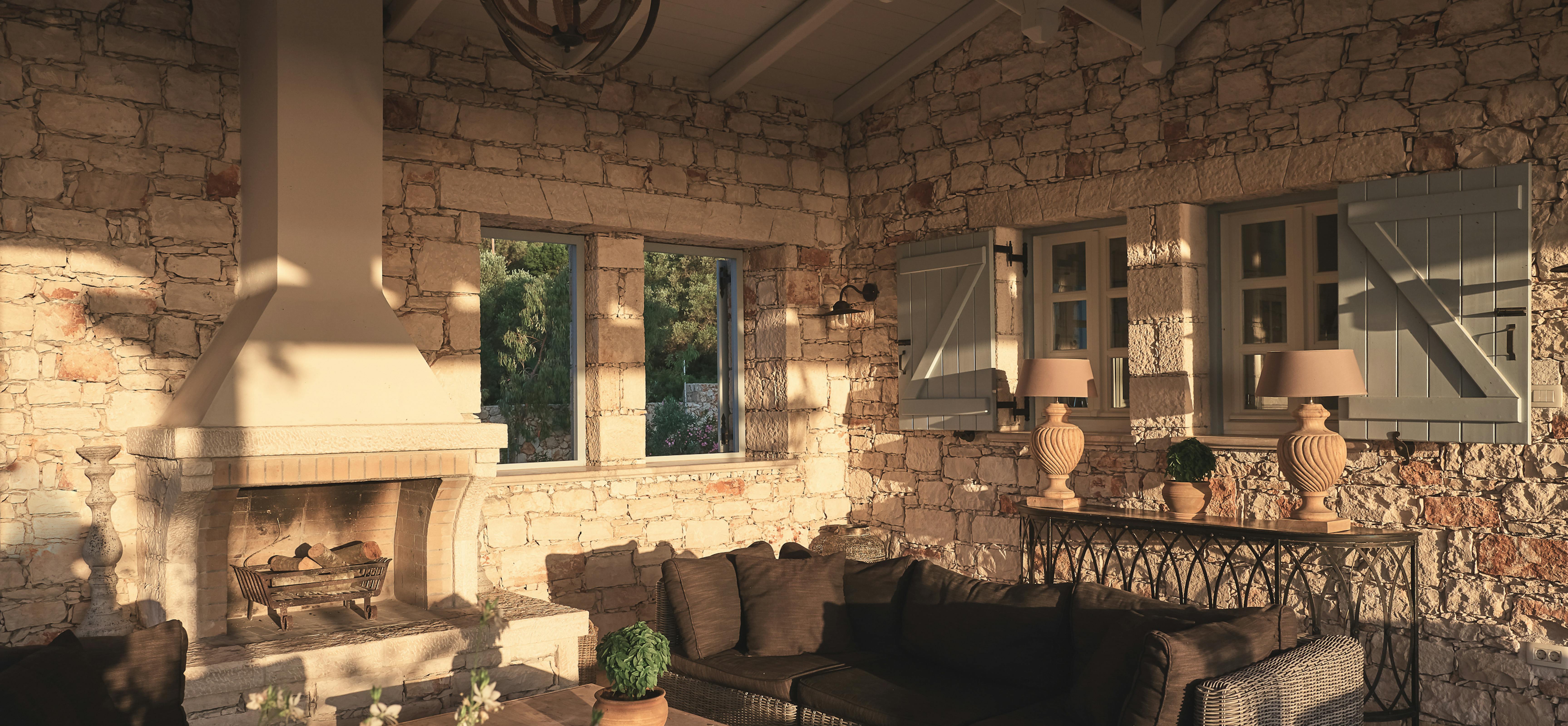 Covered outdoor living room with exposed stone walls, fireplace, and wicker furniture under vaulted ceiling.