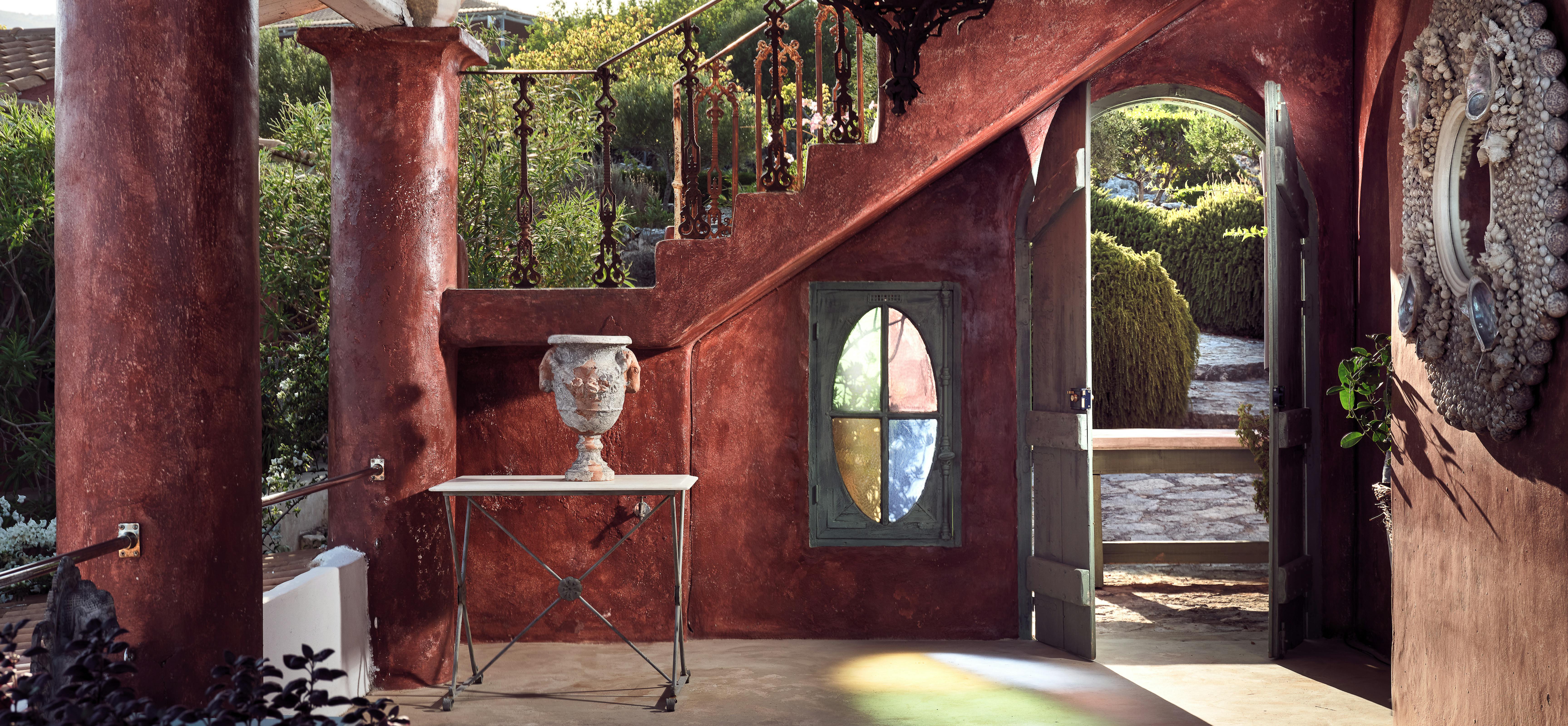 Dramatic covered entrance with rust-red walls, ornate Moroccan lantern, decorative door with stained glass oval, white console table, and carved details.