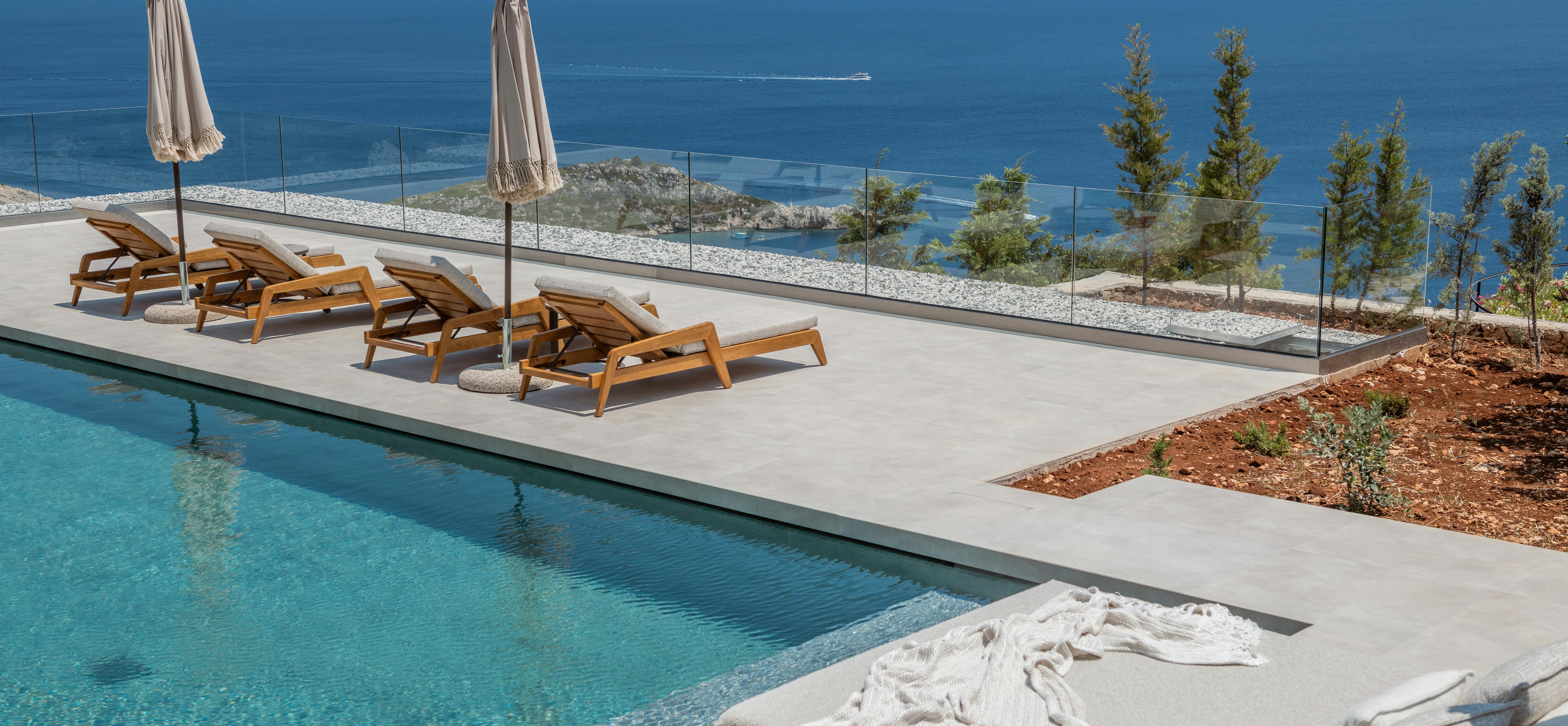 The pool area includes a glass safety railing, contemporary cushioned loungers, and an uninterrupted view of the ocean horizon.