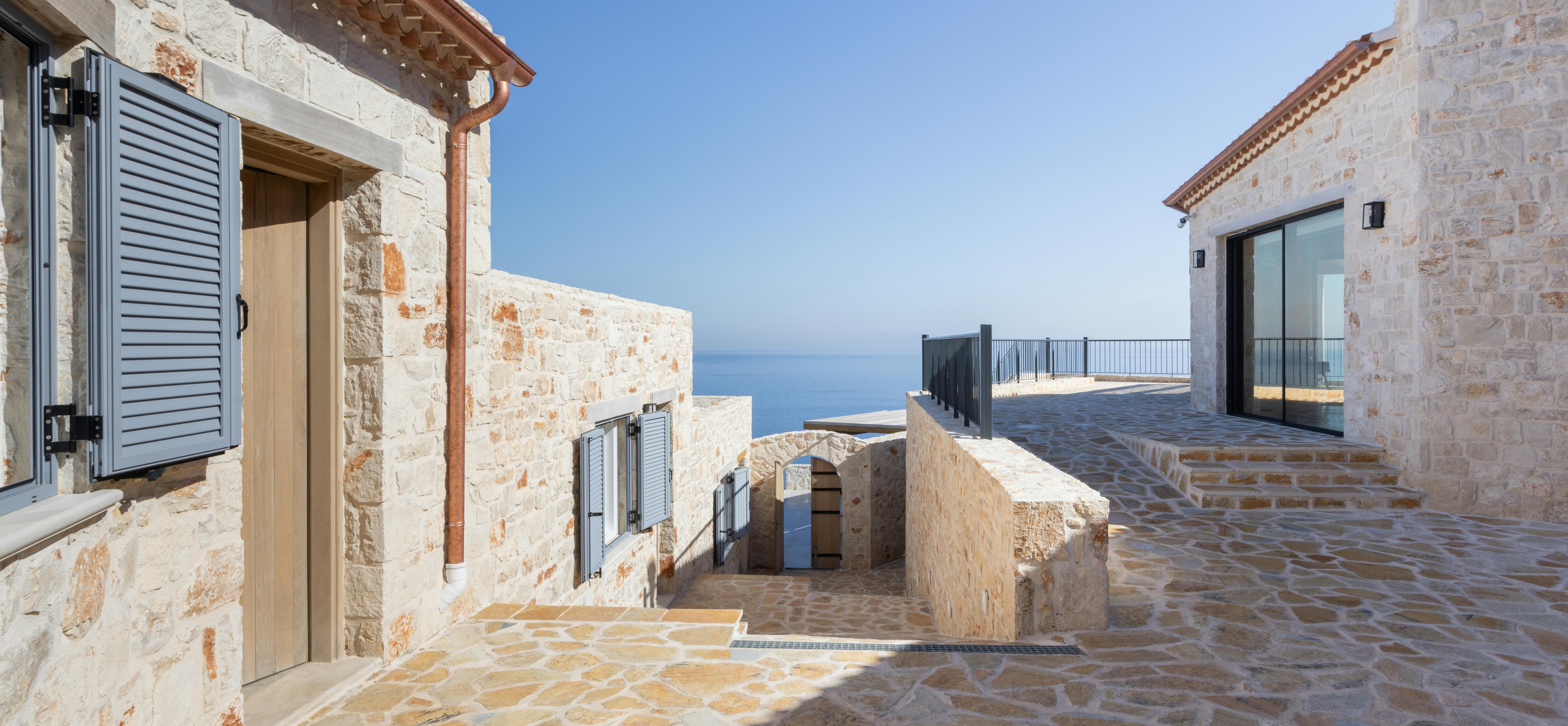 Stone courtyard with terracotta tile flooring connecting villa buildings with ocean view terrace beyond.