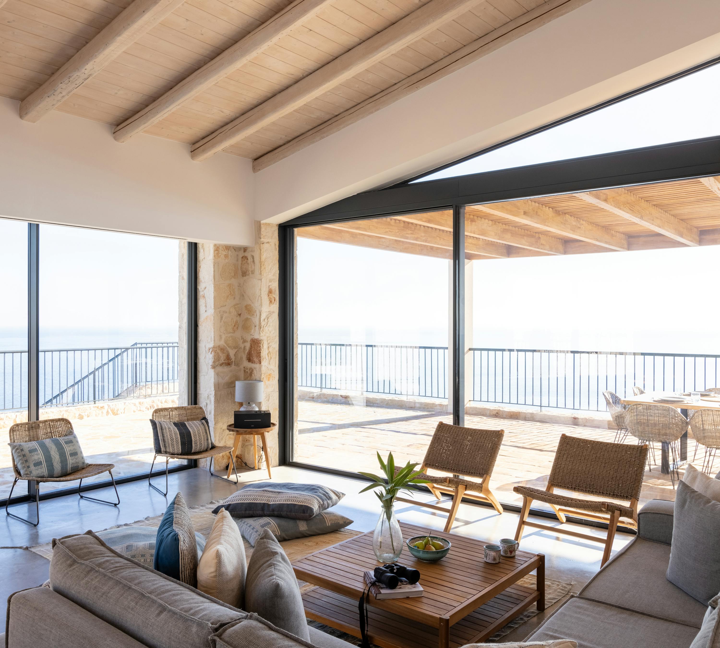 Living room with floor-to-ceiling glass doors opening to covered terrace with panoramic coastal views.