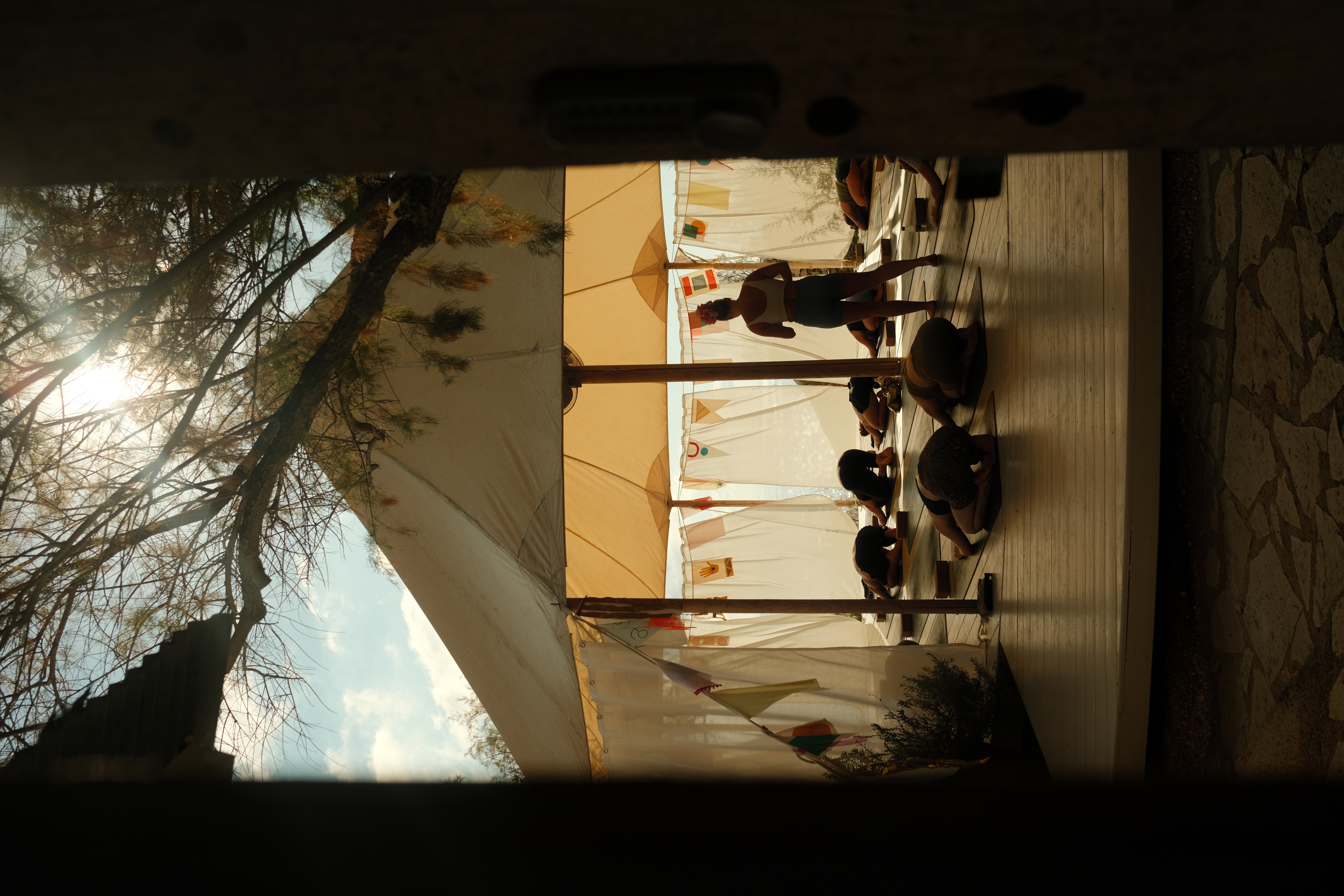 The outlines of people under a tent practicing yoga moves.