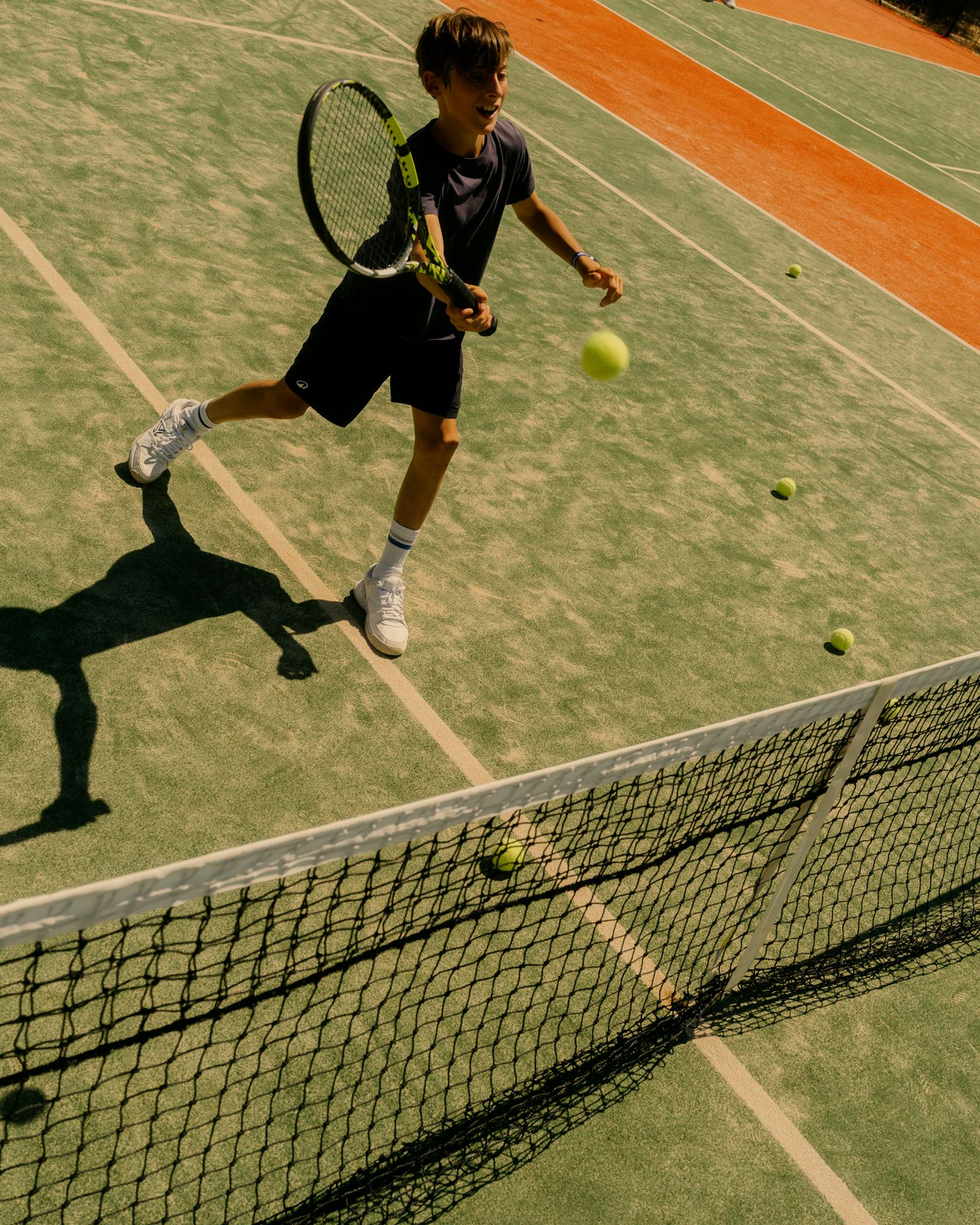 A young player mid-swing returns a shot on a sun-drenched tennis court, demonstrating focused athletic engagement in the resort's sports programming.