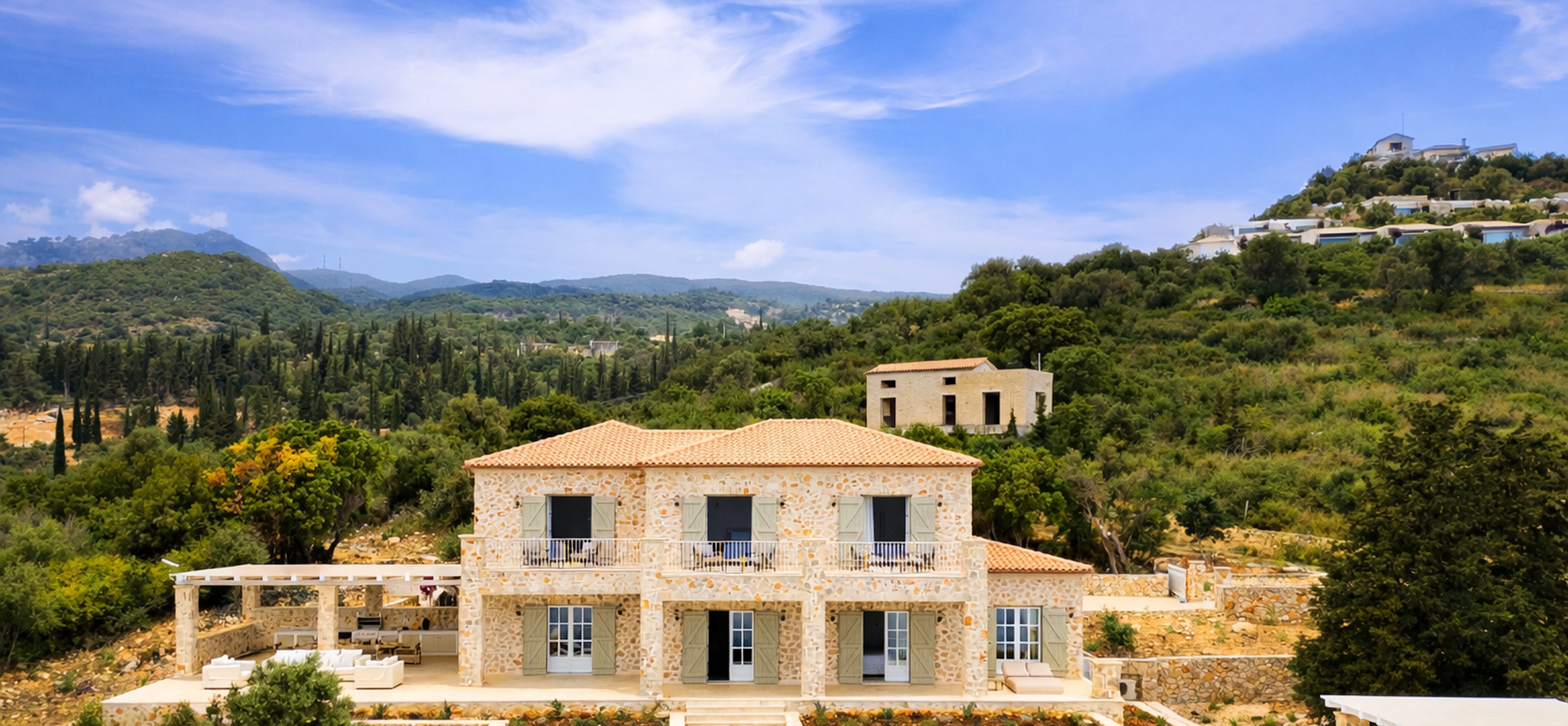 A Mediterranean-style stone villa with terracotta roof tiles sits among rolling hills, featuring a pristine swimming pool with white loungers and terraced stone walls. The property blends traditional architecture with modern luxury amenities in a scenic hillside setting.