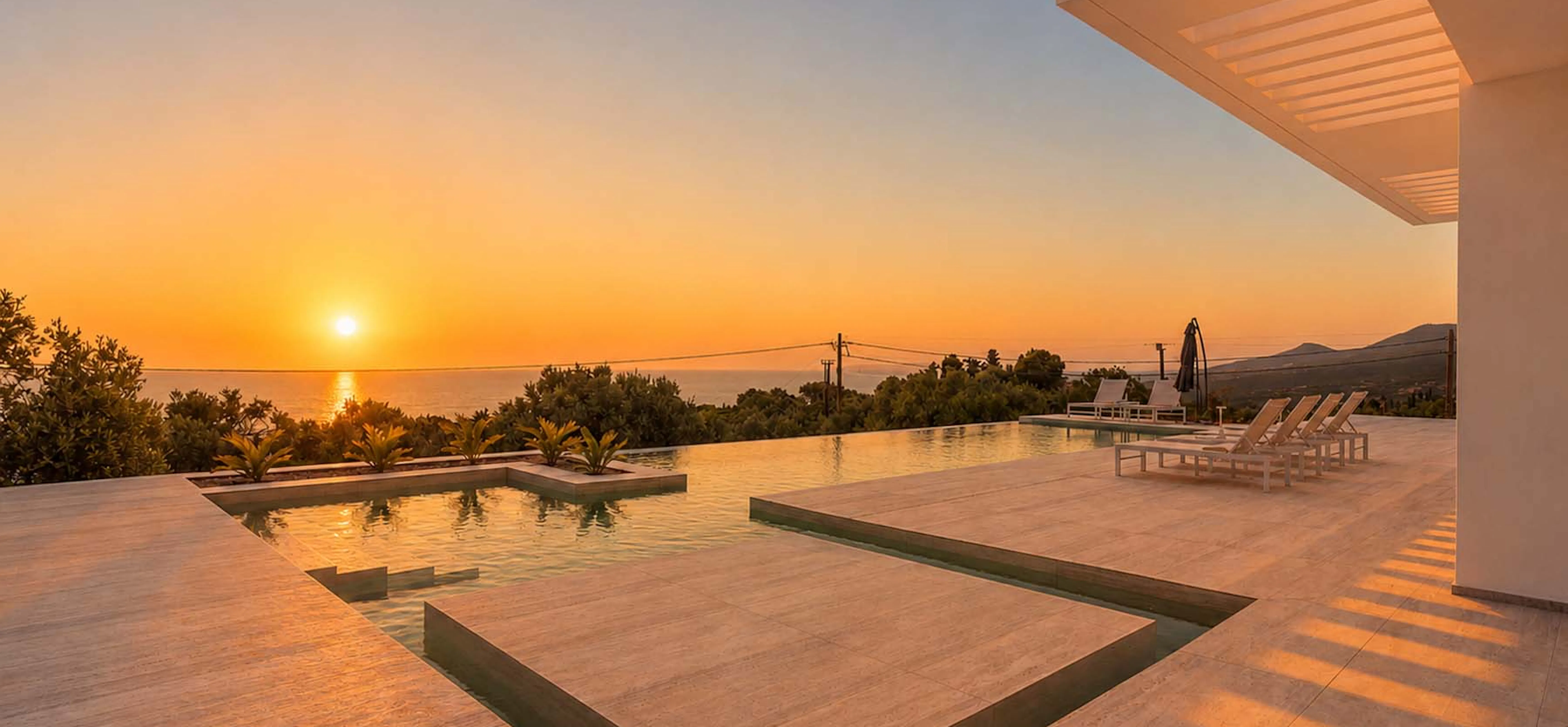 Infinity pool terrace at golden hour, pool and stepped wading area reflecting the sunset, white sun loungers to the right, with the villa pergola framing the scene