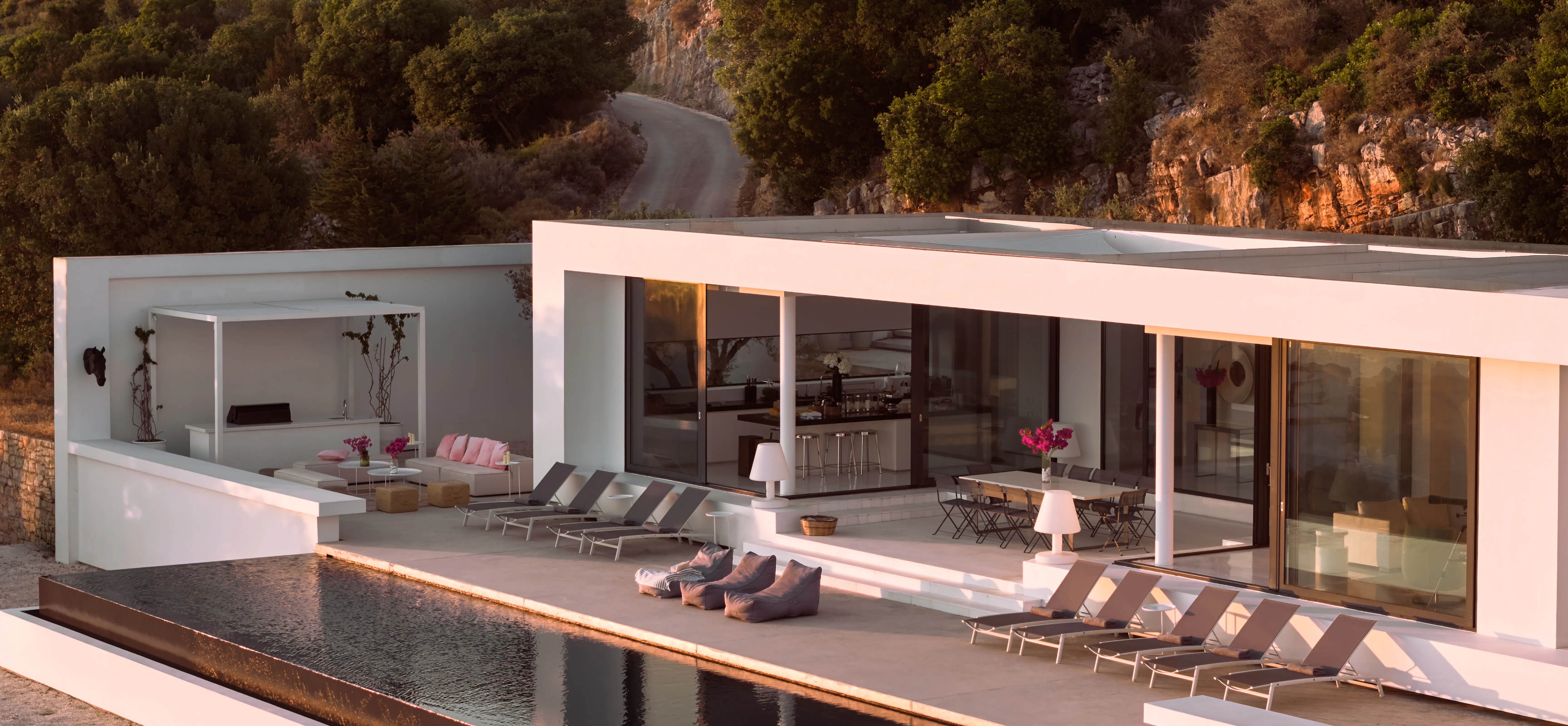 Aerial view of the villa's pool terrace, showing loungers, outdoor dining, and the property layout amid green hills