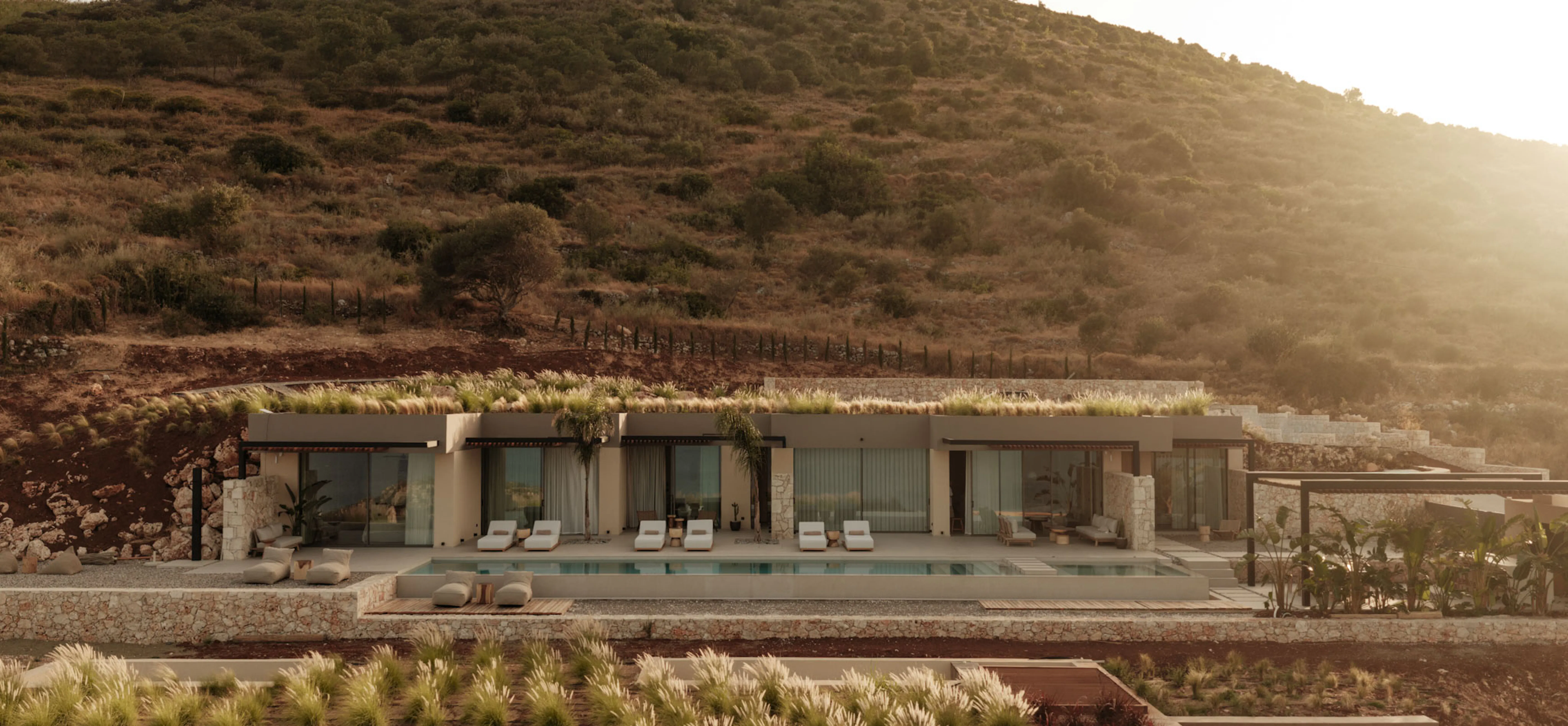 Golden-hour view of The Upper House's pool wing with sun loungers along the water and hills rising behind