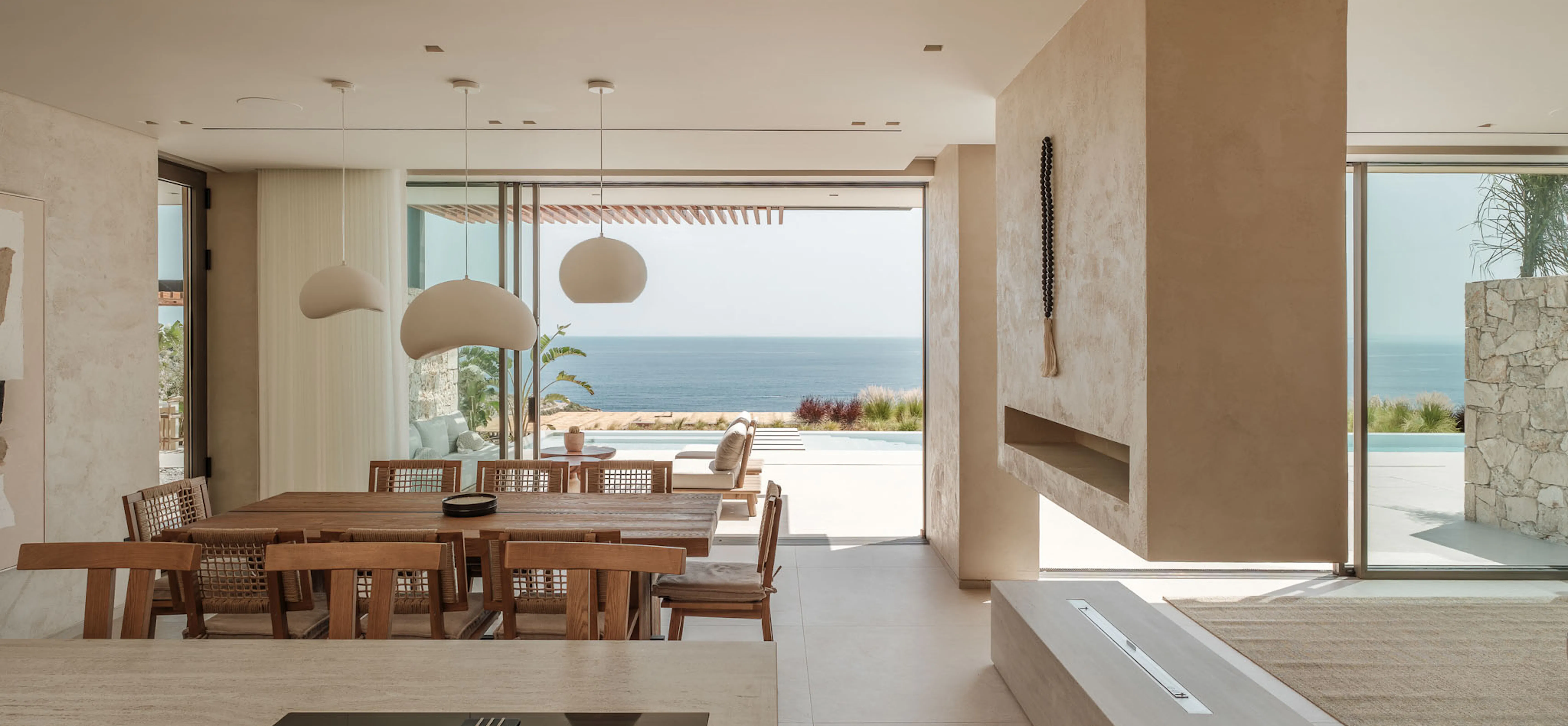 Open-plan interior with a dining area and lounge space divided by a low wall, dark tiled flooring, and a sea view beyond.