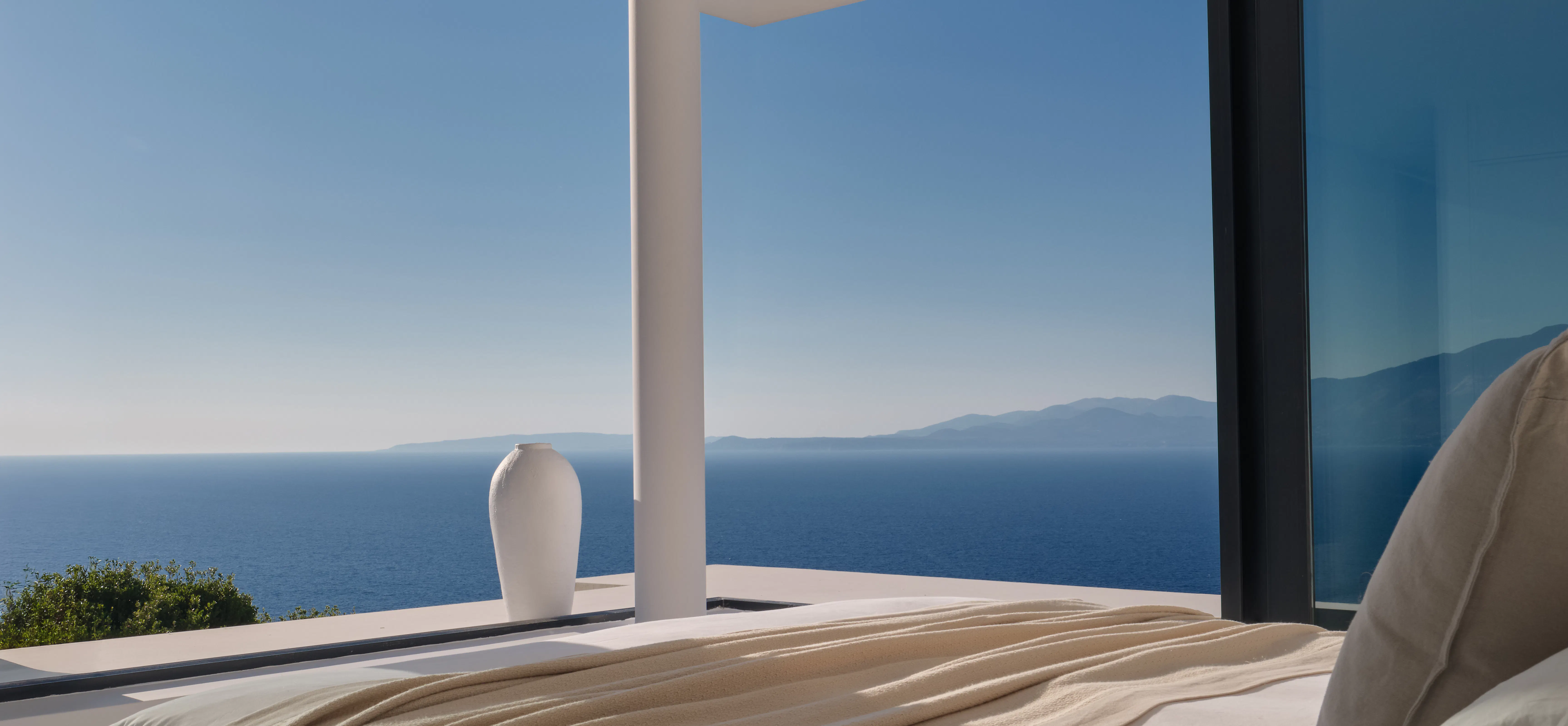 Bedroom detail with a white ceramic vase on the terrace ledge beside the bed, framed by a column and sea view